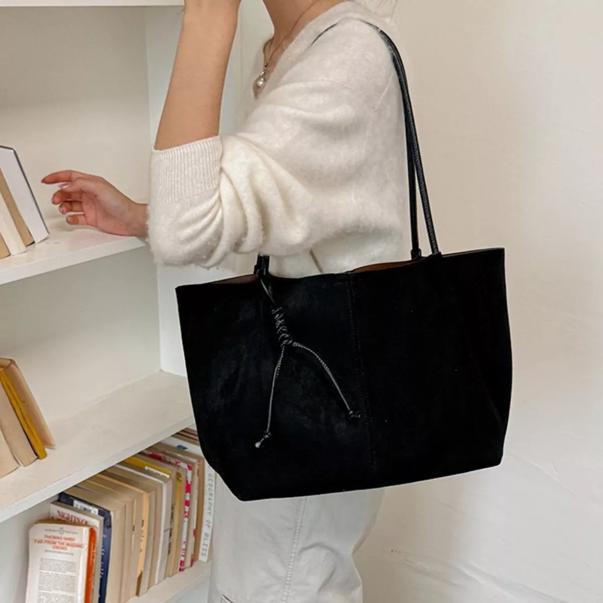 Black suede tote bag carried on shoulder with two top handles and front drawstring pocket