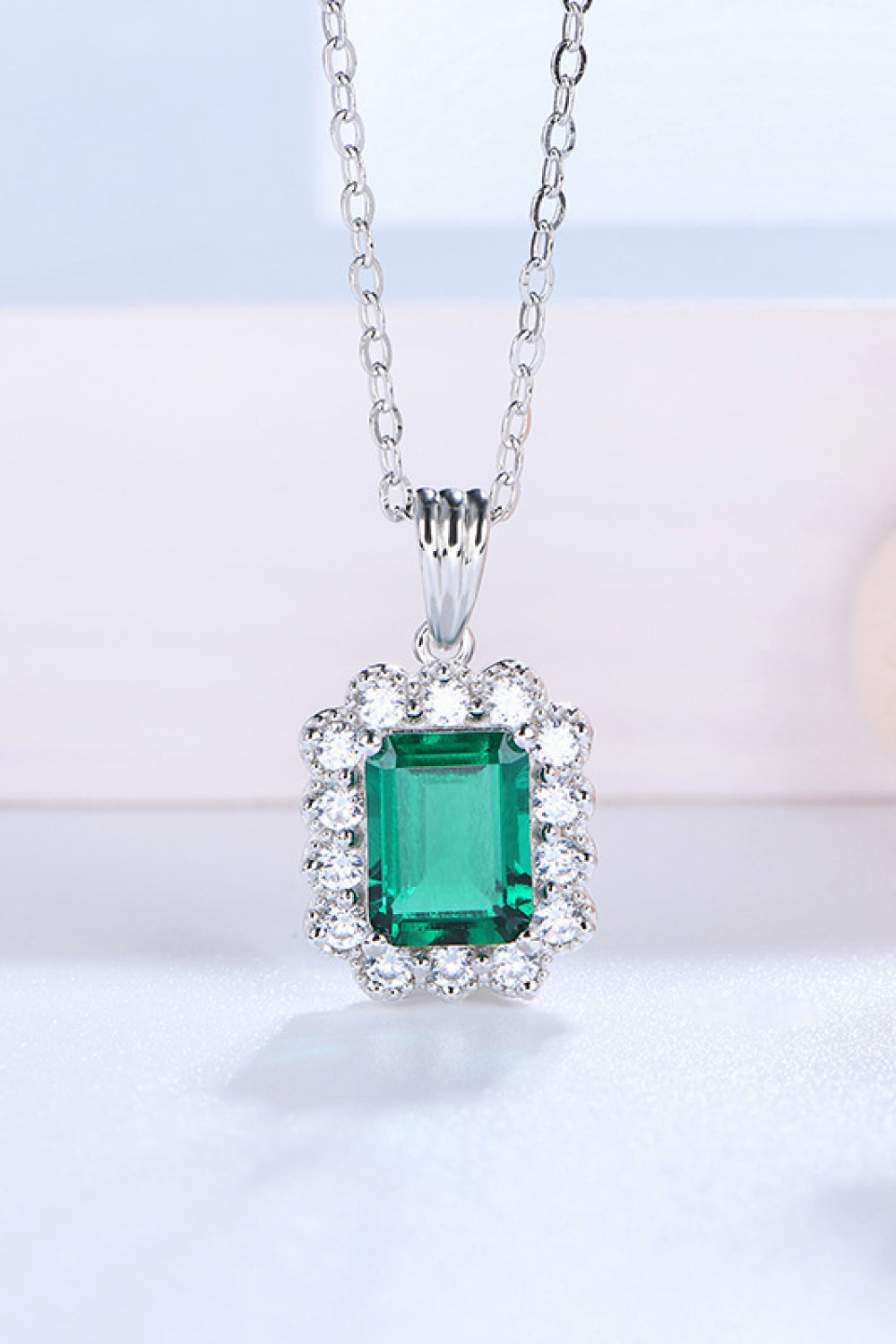 Emerald pendant necklace with square green center stone and round diamond halo, silver chain