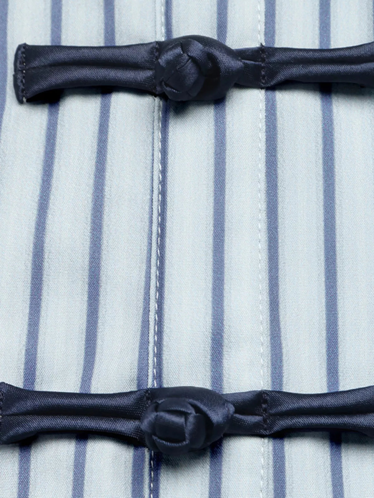 Striped shirt placket detail with two black knot closures on blue-and-white vertical stripes