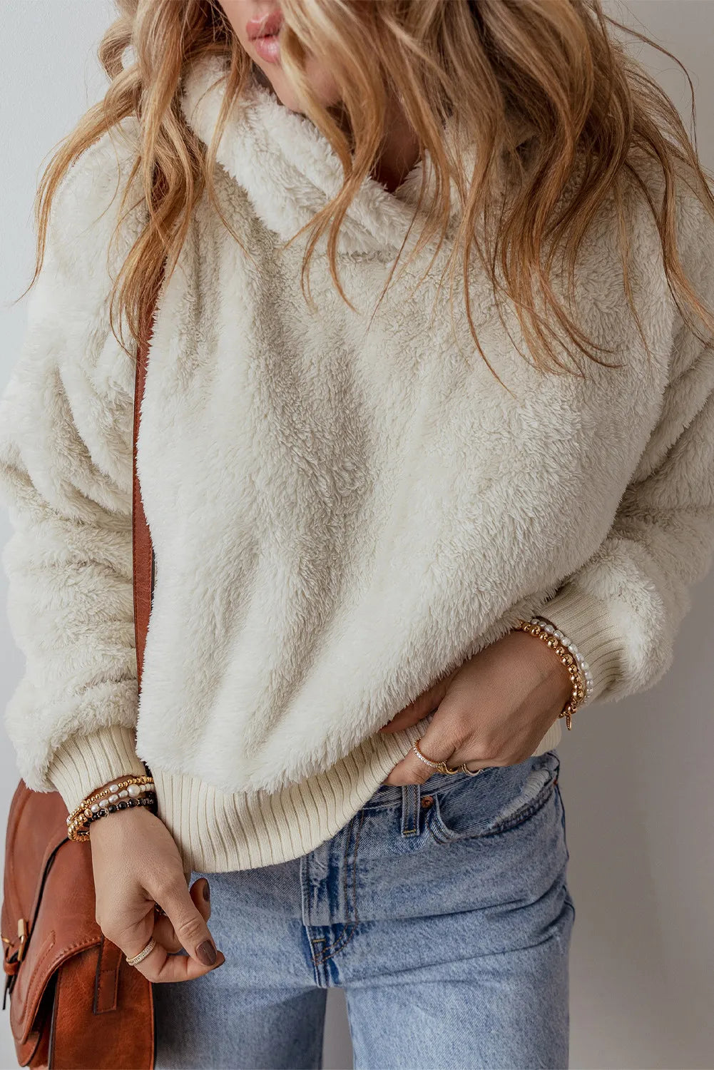 Beige fuzzy long-sleeve hoodie with hood and ribbed cuffs, side view worn with jeans