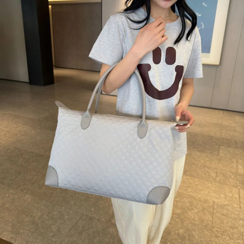 Light-colored quilted travel bag with top handles, side pulls, and zip top