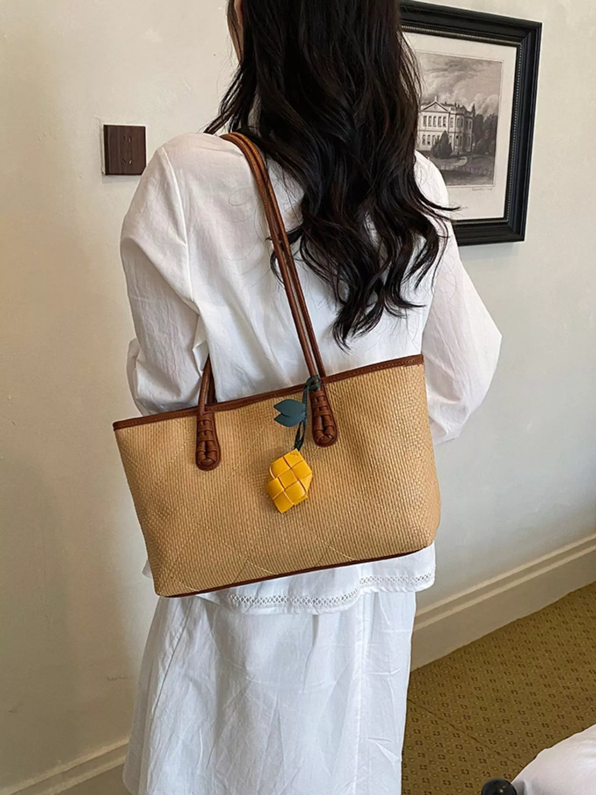 Beige leather shoulder bag worn on shoulder with brown handles and yellow charm