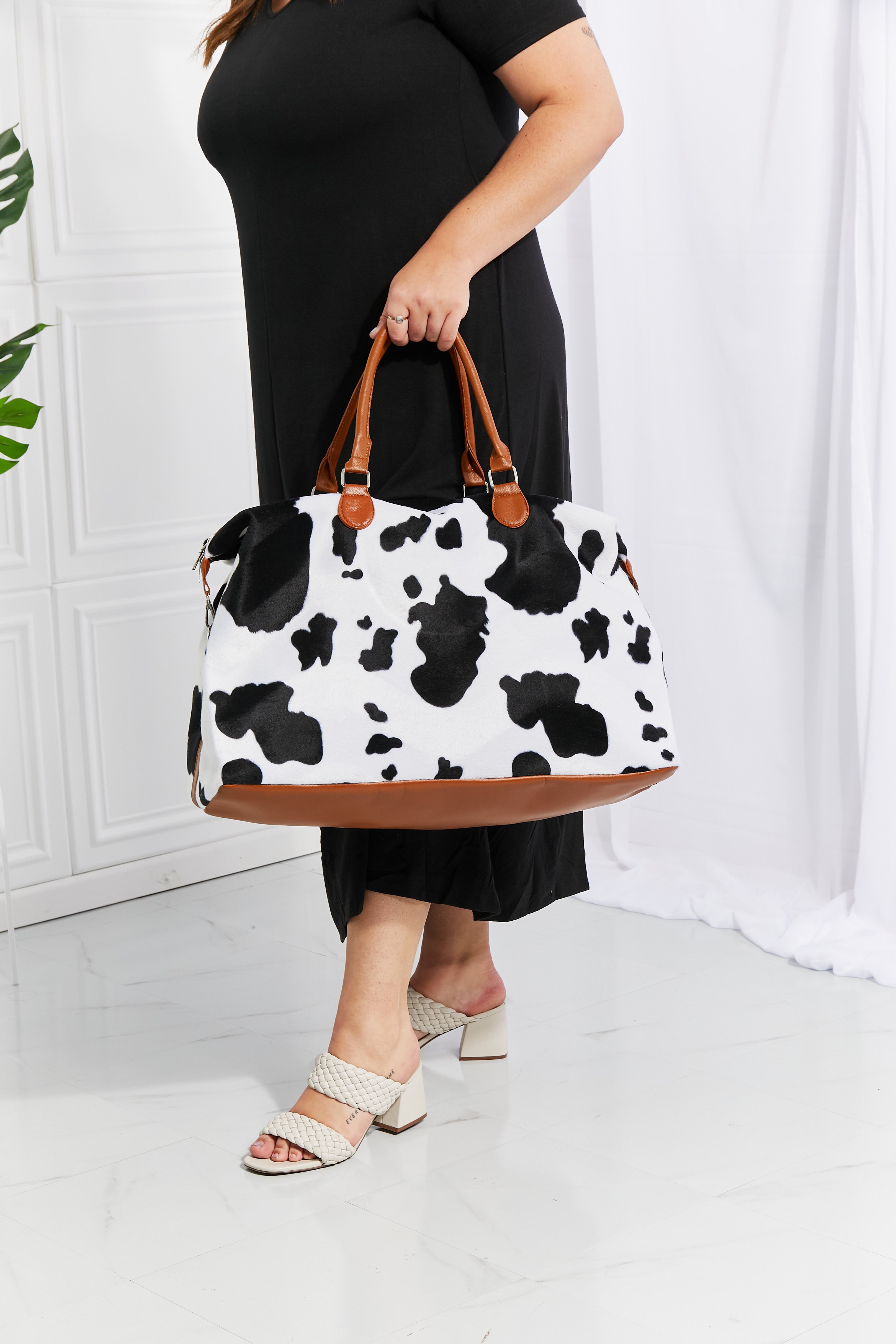 Cow print plush weekender bag with tan handles, wide base, and zip closure