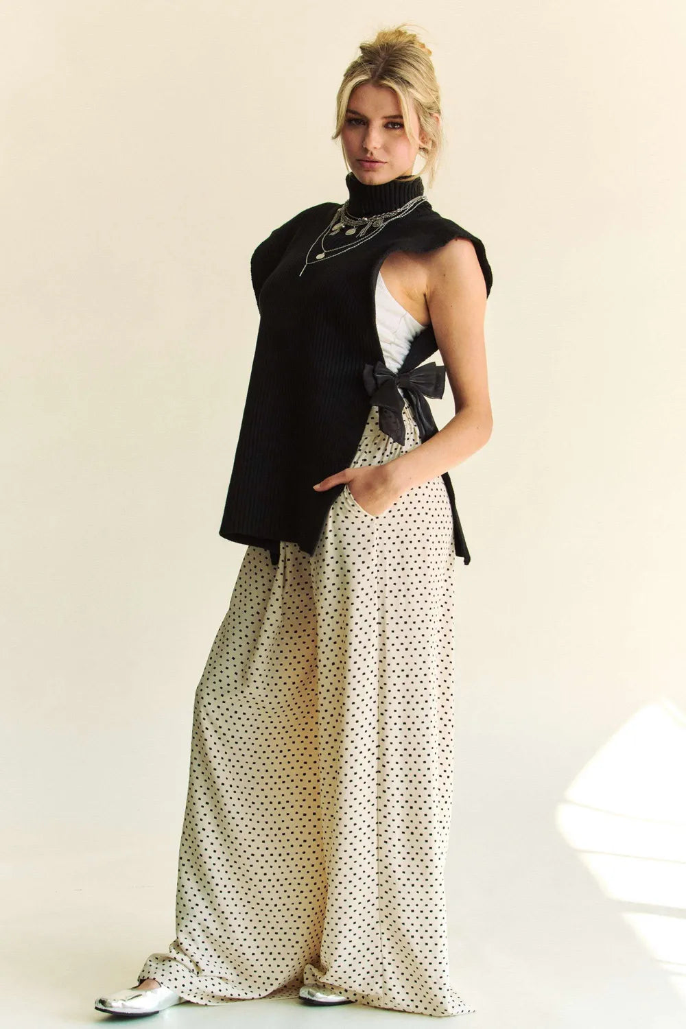 Black sleeveless knit turtleneck top with side slit and bow accent