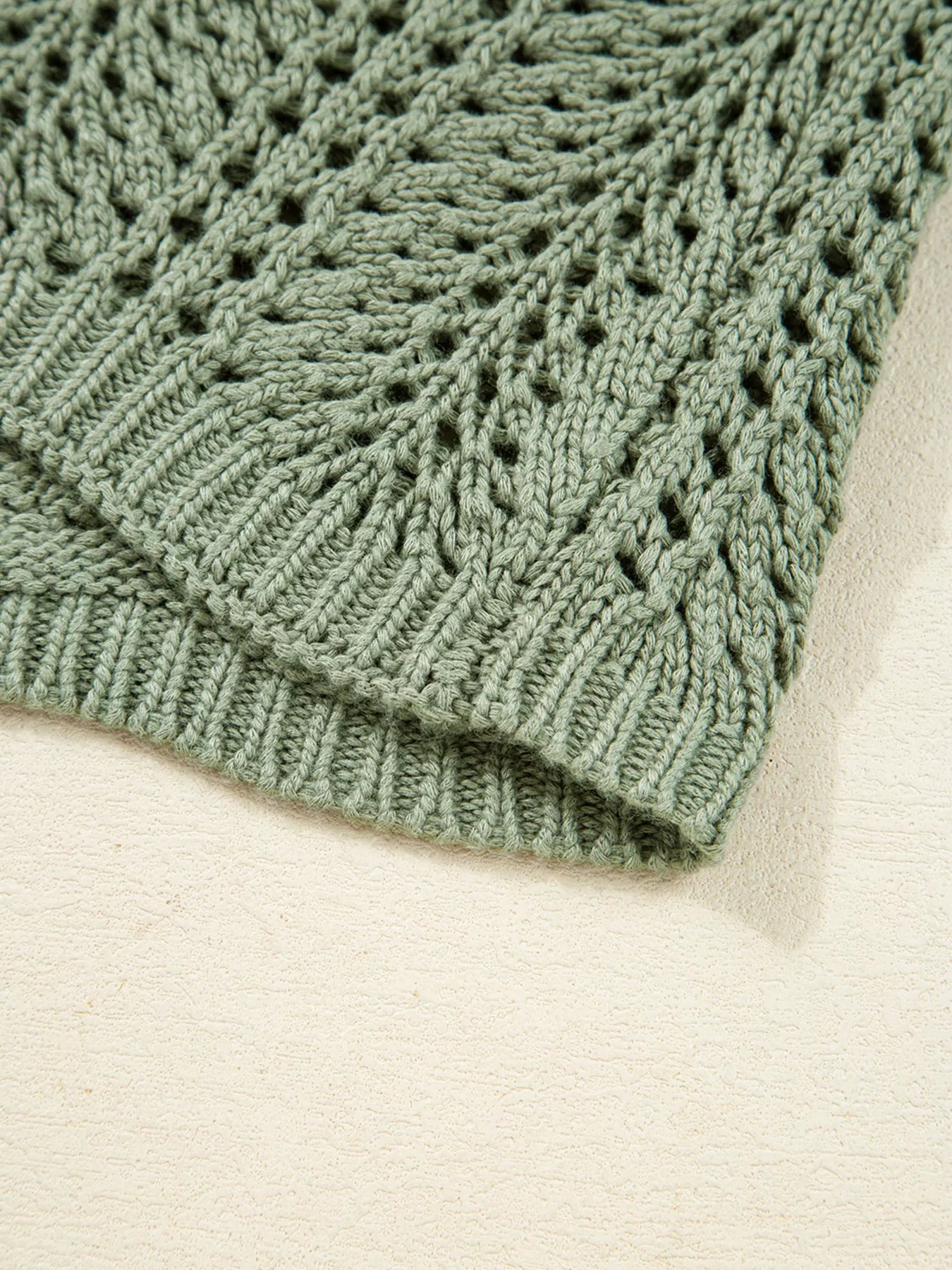 Sage eyelet knit cardigan hem with ribbed trim and openwork stitch texture.