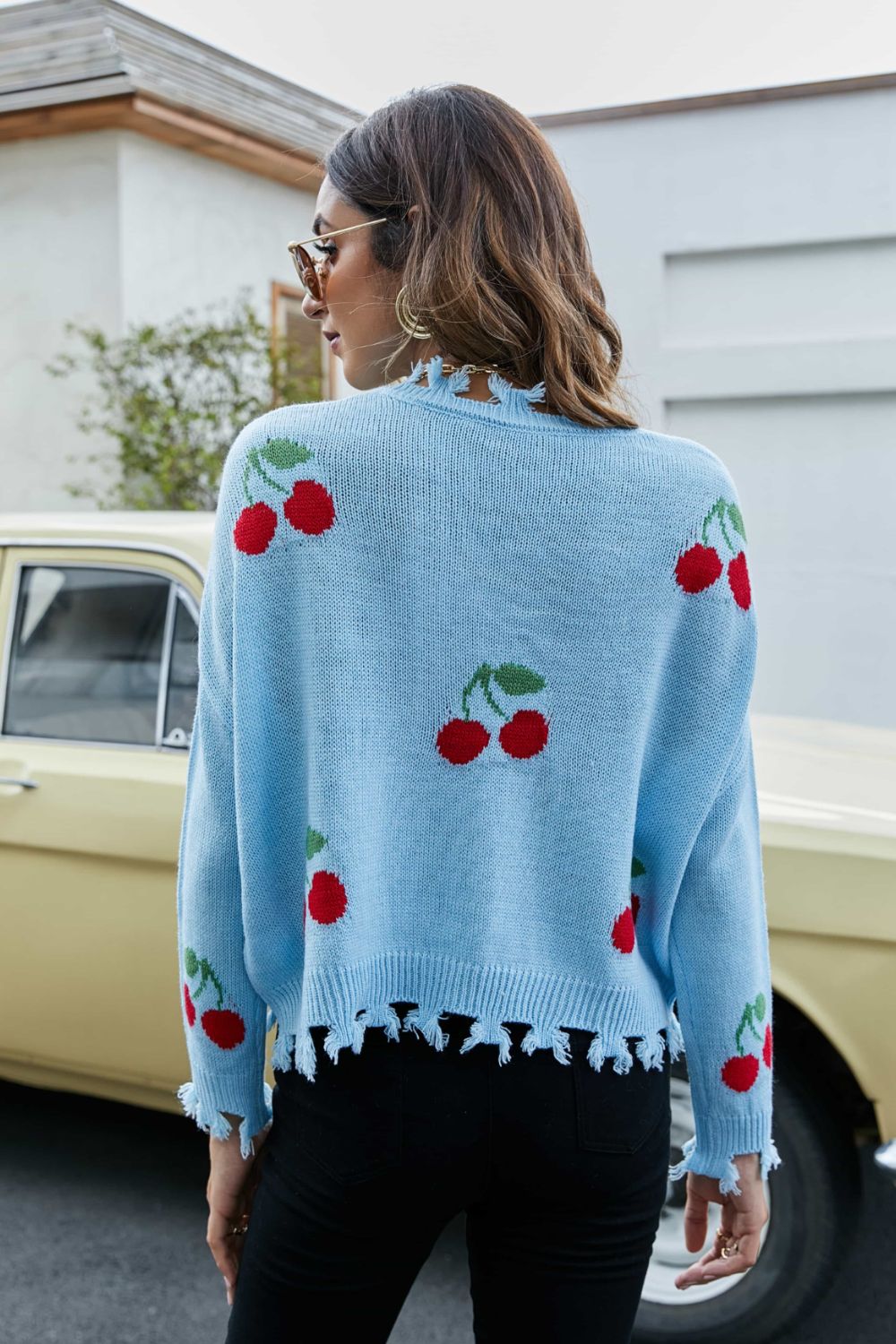 Back view of sky blue V-neck sweater with cherry print and frayed hem trim