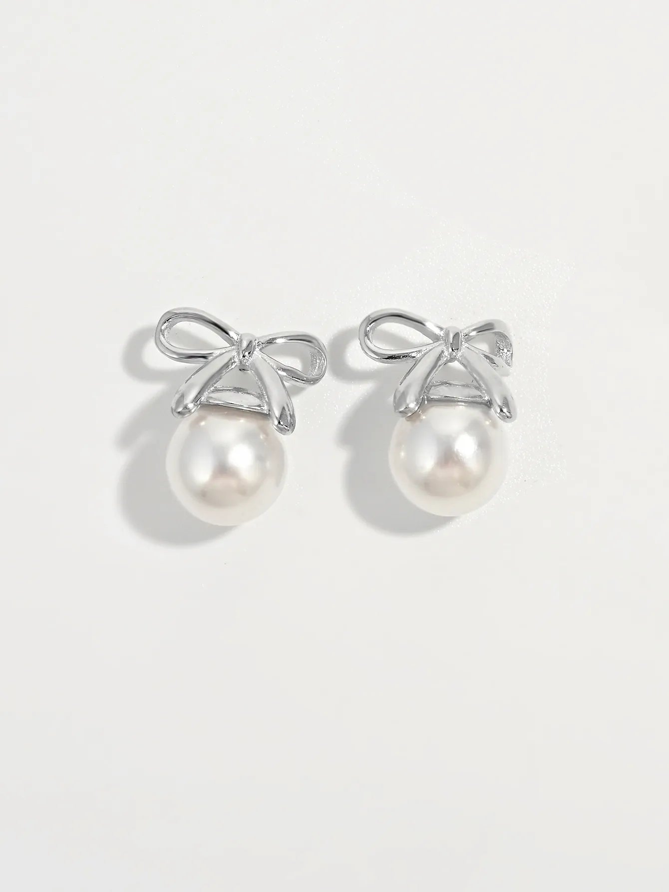 Silver bow stud earrings with round white pearls, matching pair.