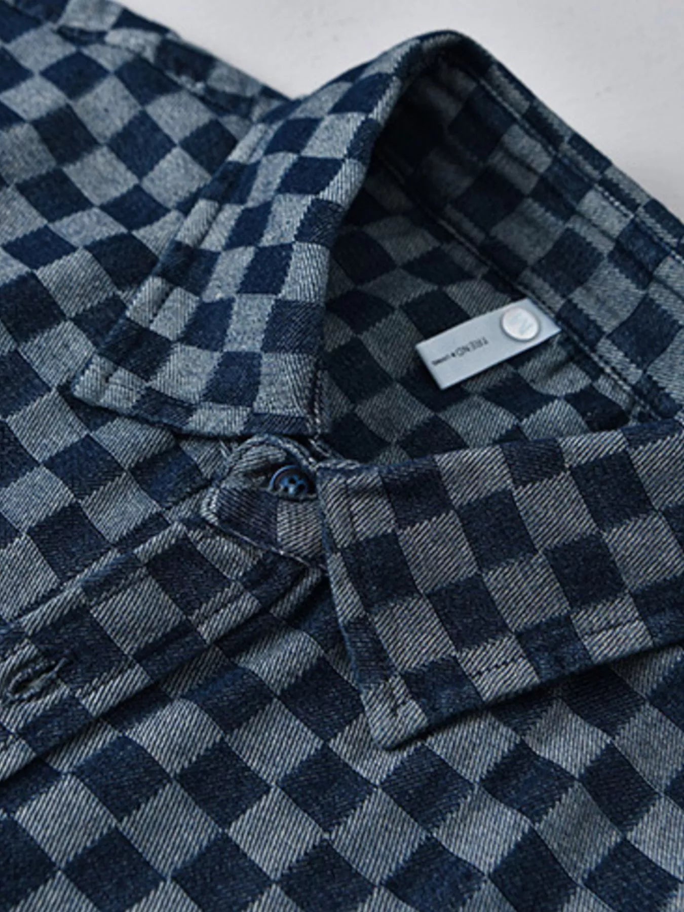 Button-front and neck label detail on a blue checkered short-sleeve shirt