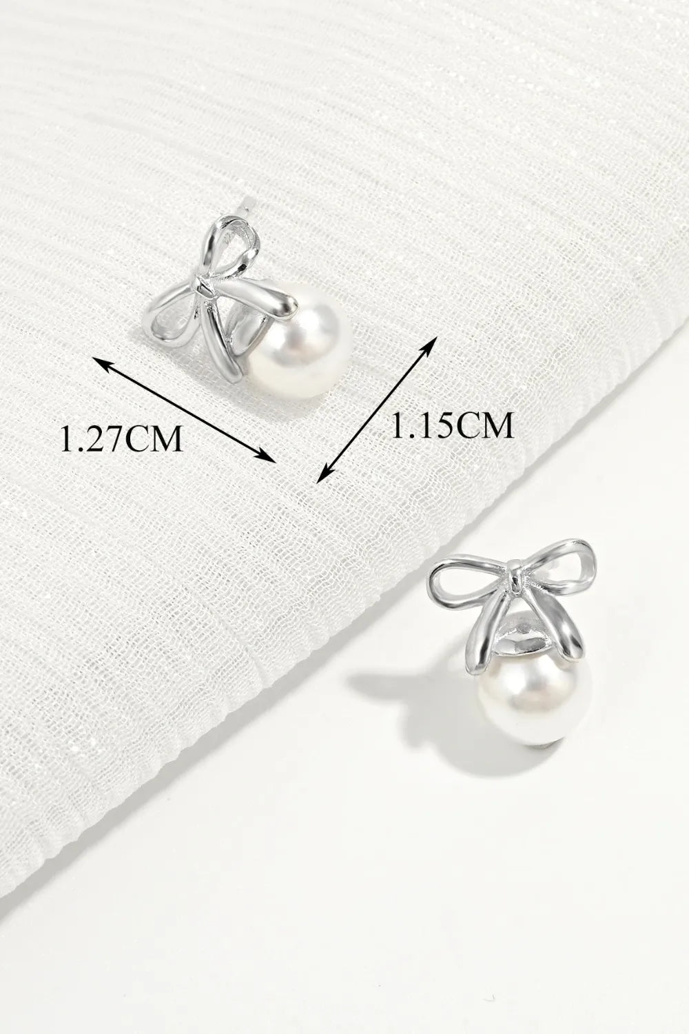Silver bow stud earrings with pearl drops; size shown as 1.27 cm and 1.15 cm.