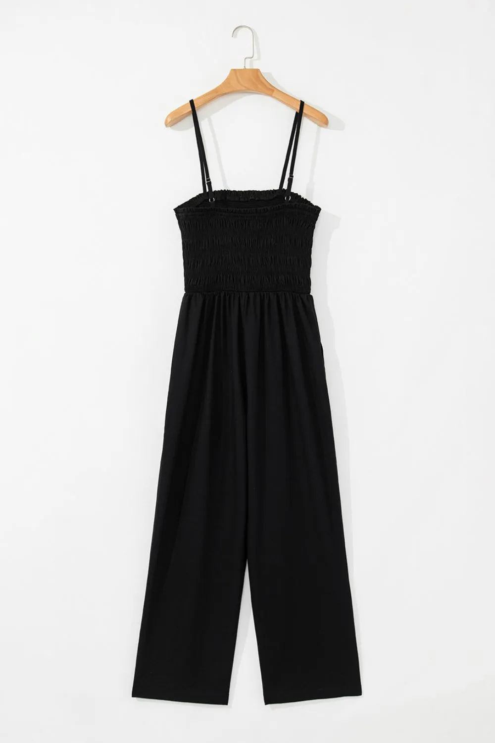 Black smocked spaghetti strap wide-leg jumpsuit on a hanger, angled front view