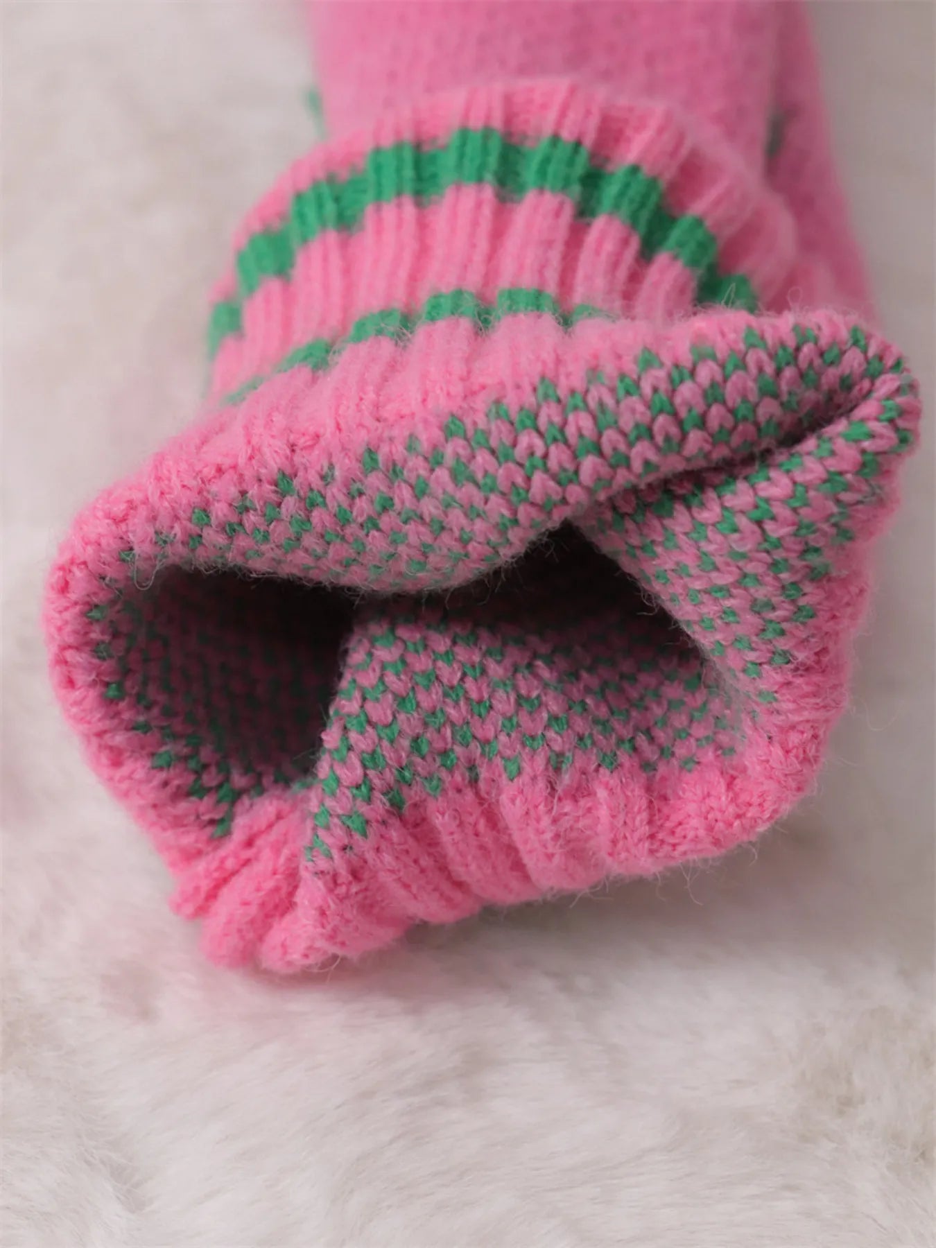 Pink sweater sleeve cuff with green-striped ribbing and textured knit