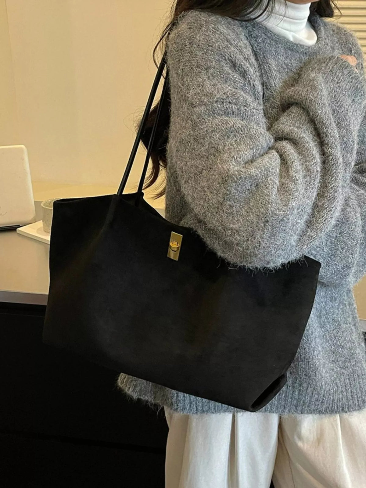 Black suede tote bag worn on shoulder, gold turn-lock clasp, top handles