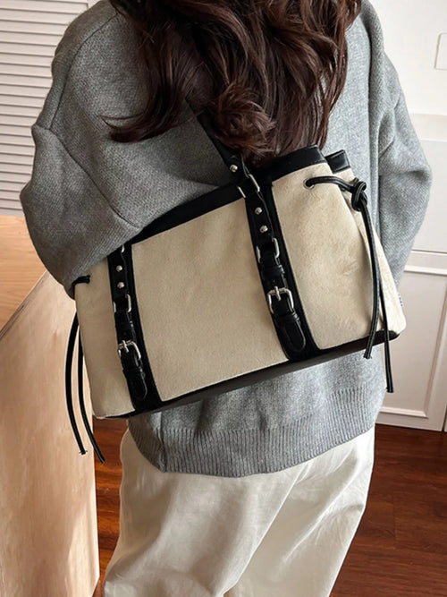 Cream tote bag with black handles, rivets, and buckle front detail