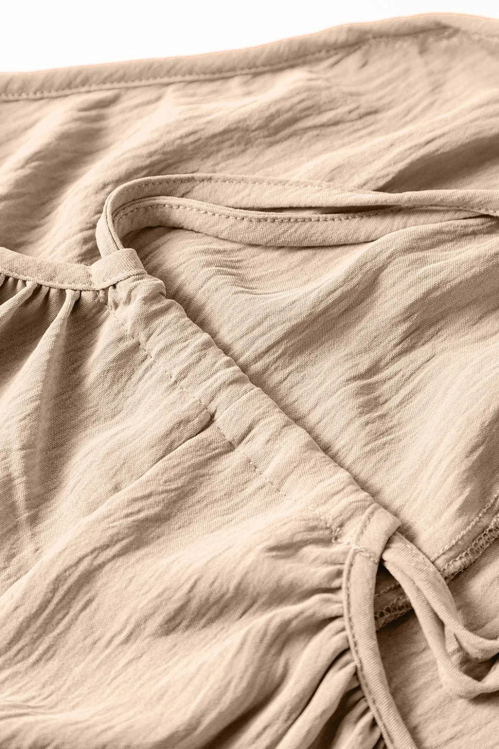 Khaki jumpsuit fabric close-up with gathered seam and tie detail