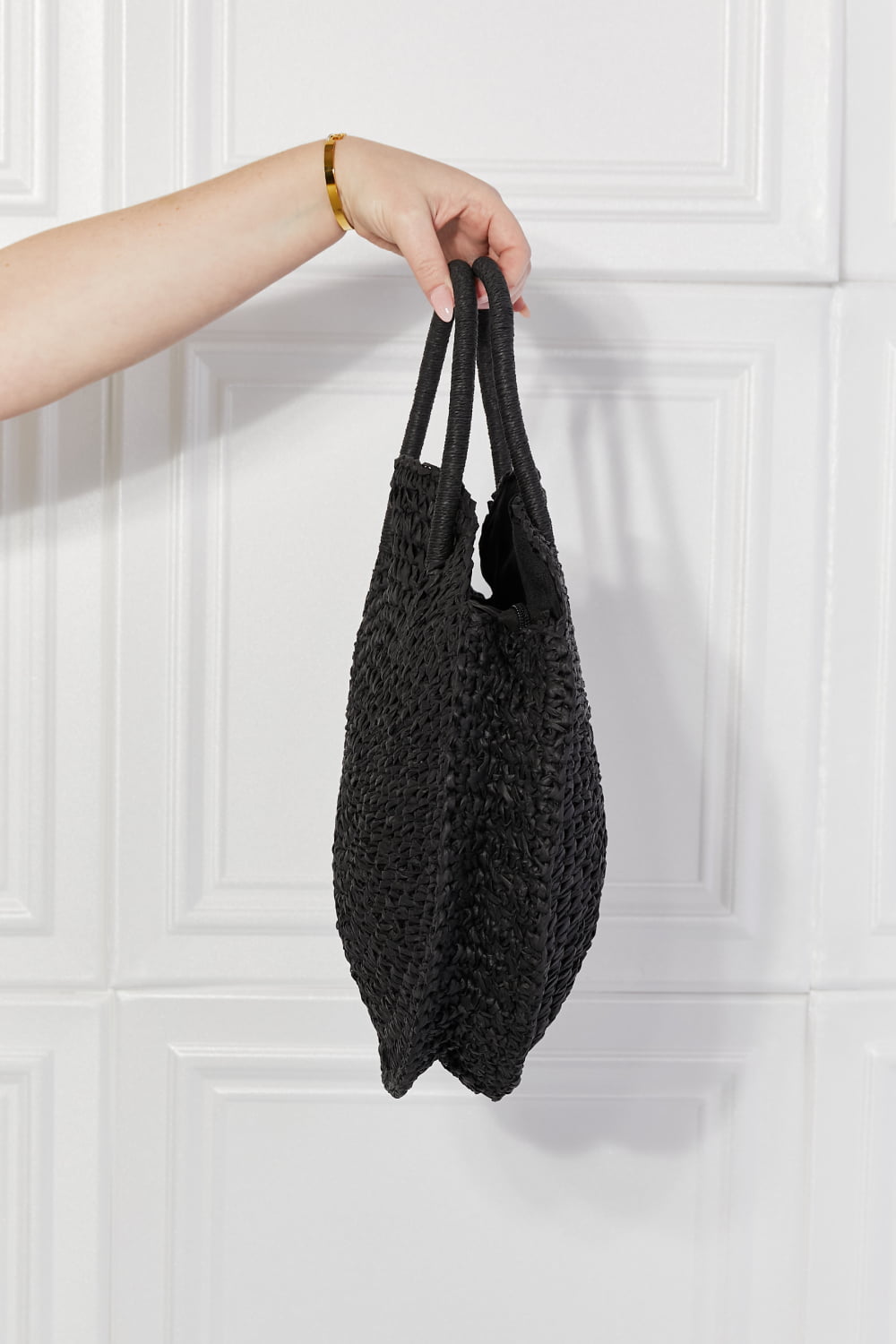 Black round woven straw rattan handbag with elongated handle loops, side view