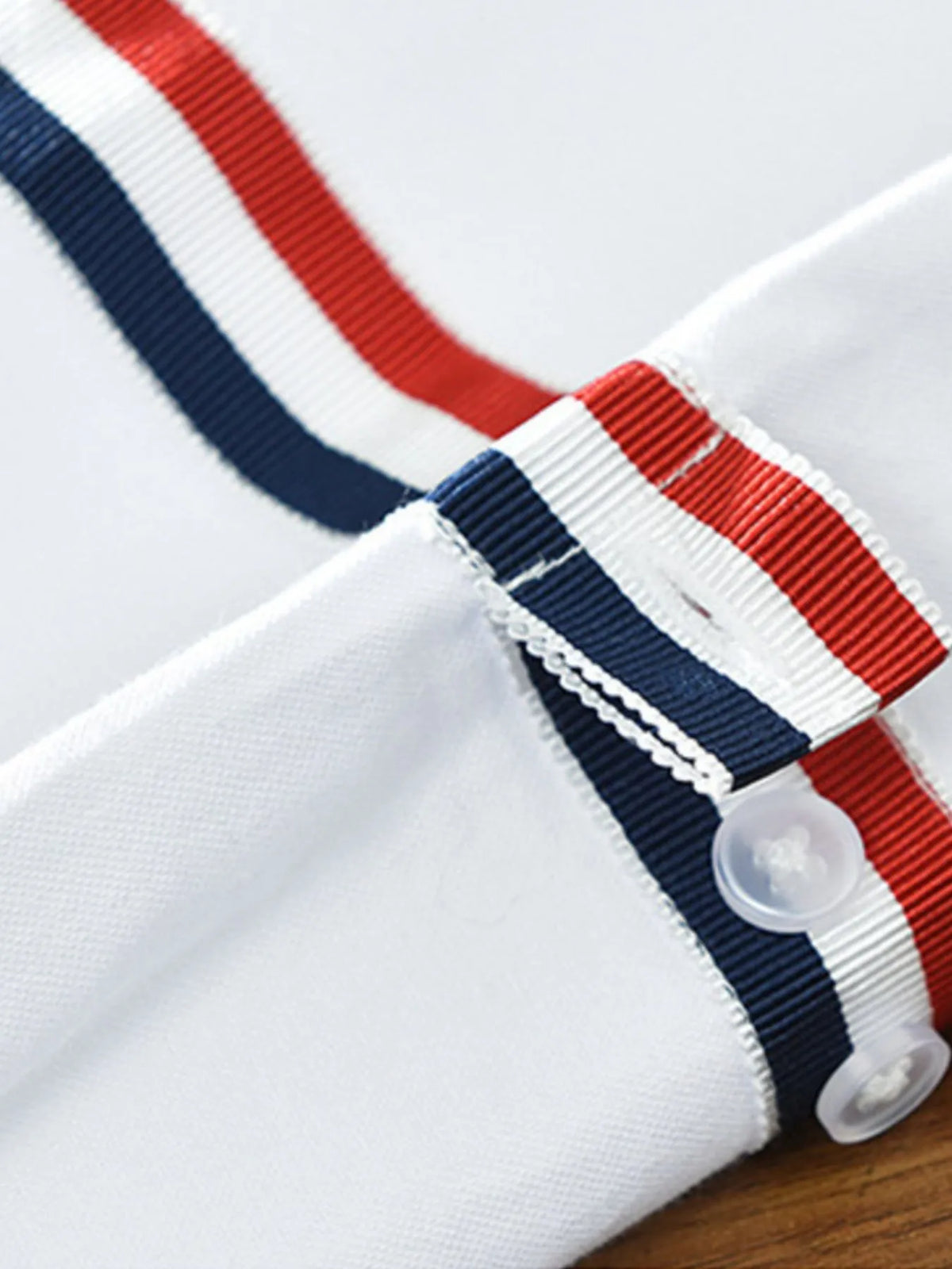 Men's shirt cuff detail with red and navy striped band and white buttons