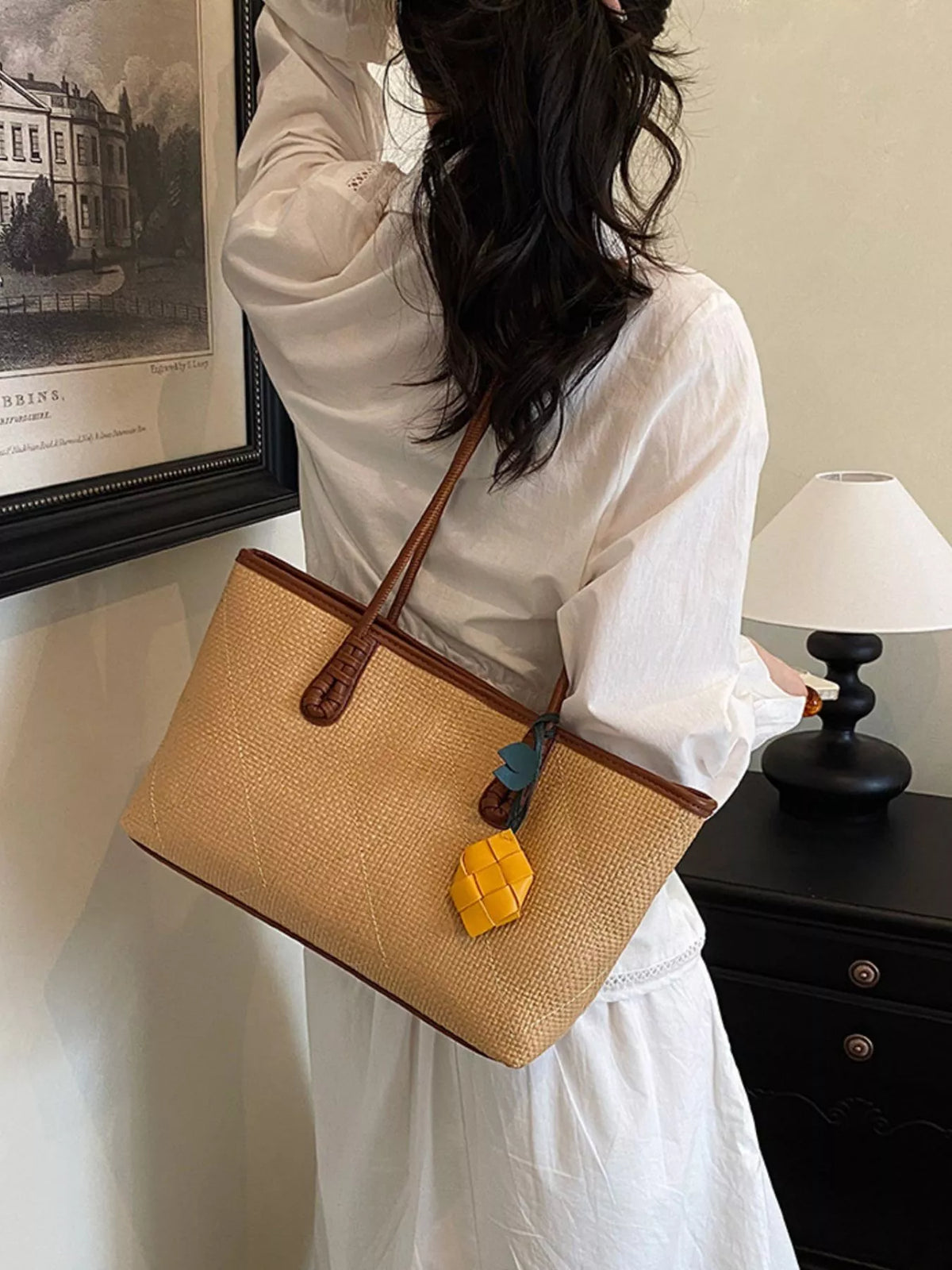 Beige leather shoulder bag on shoulder with brown handles and yellow charm detail