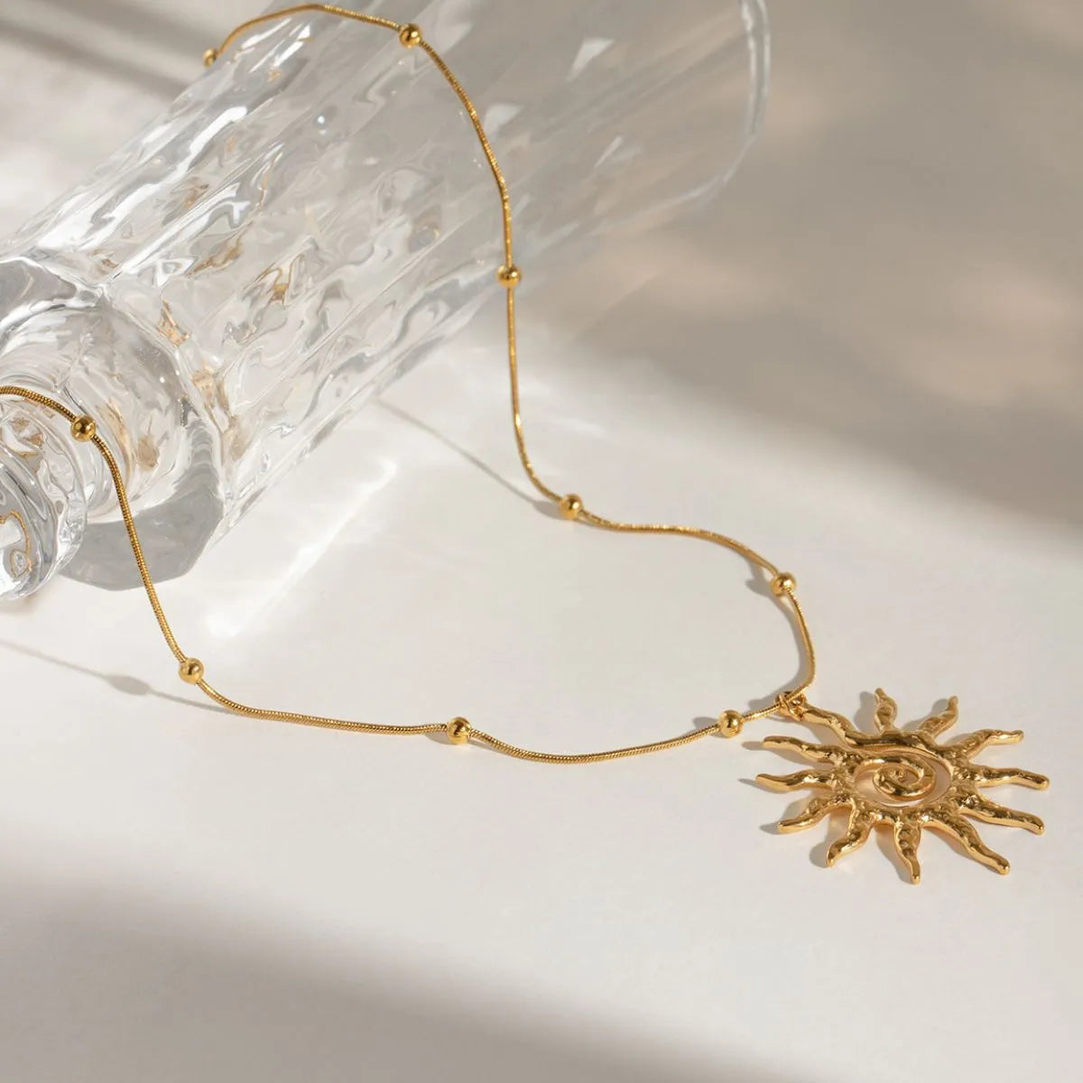 Gold-plated sun pendant necklace draped with delicate chain and sun swirl charm