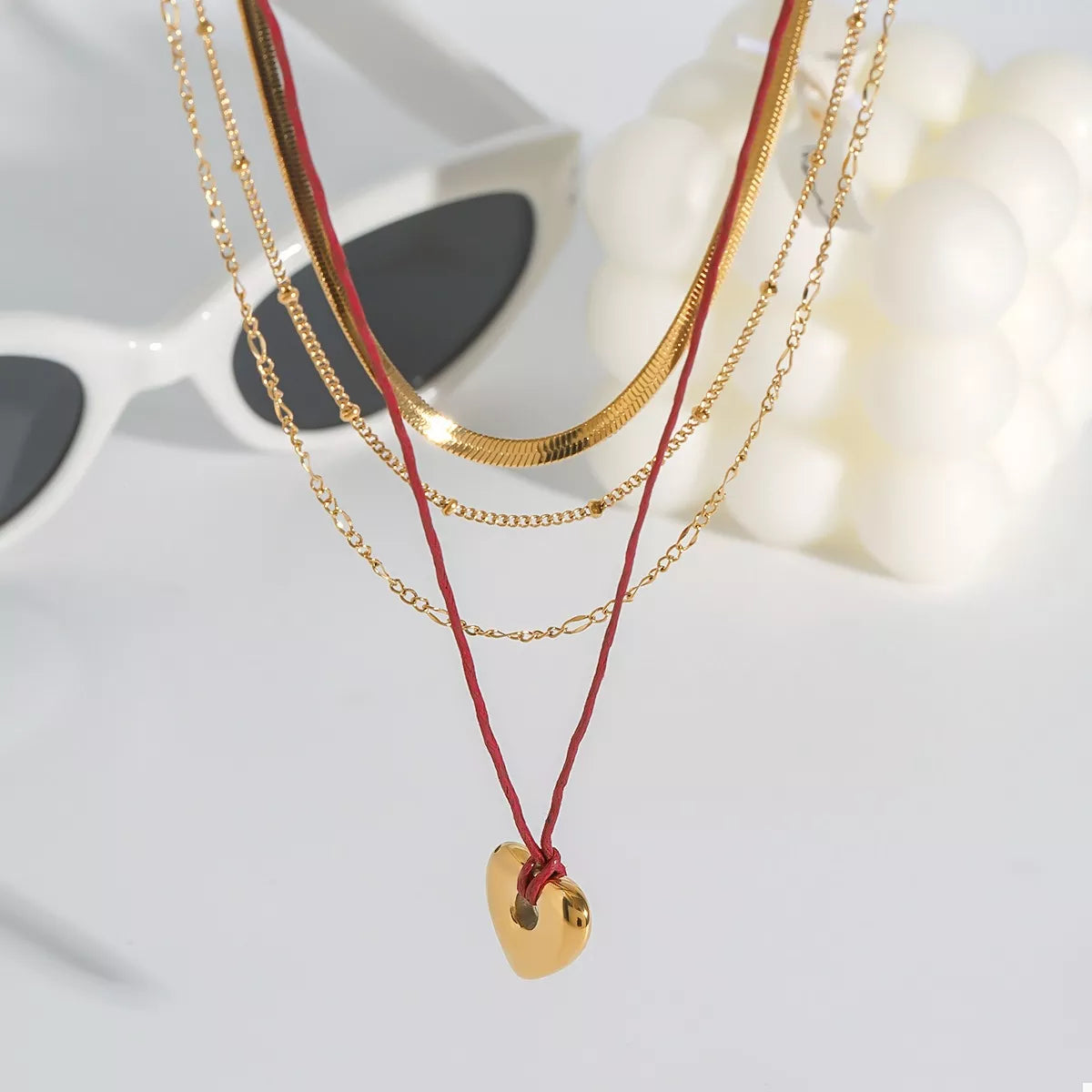 Layered gold heart necklace with red cord; gold heart pendant near center, product shot.