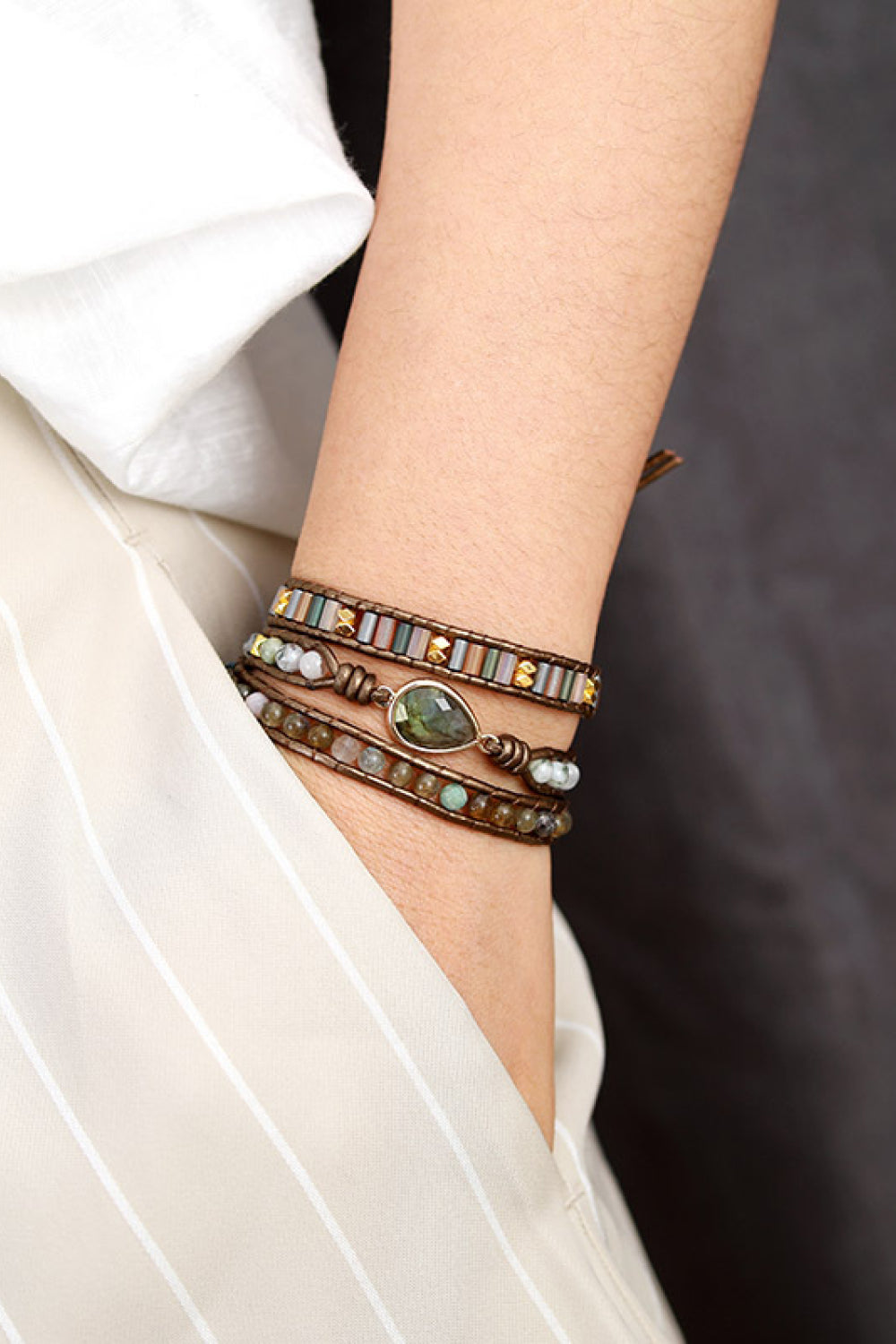 Triple-layer beaded bracelet on wrist with brown wrap and green stone accents