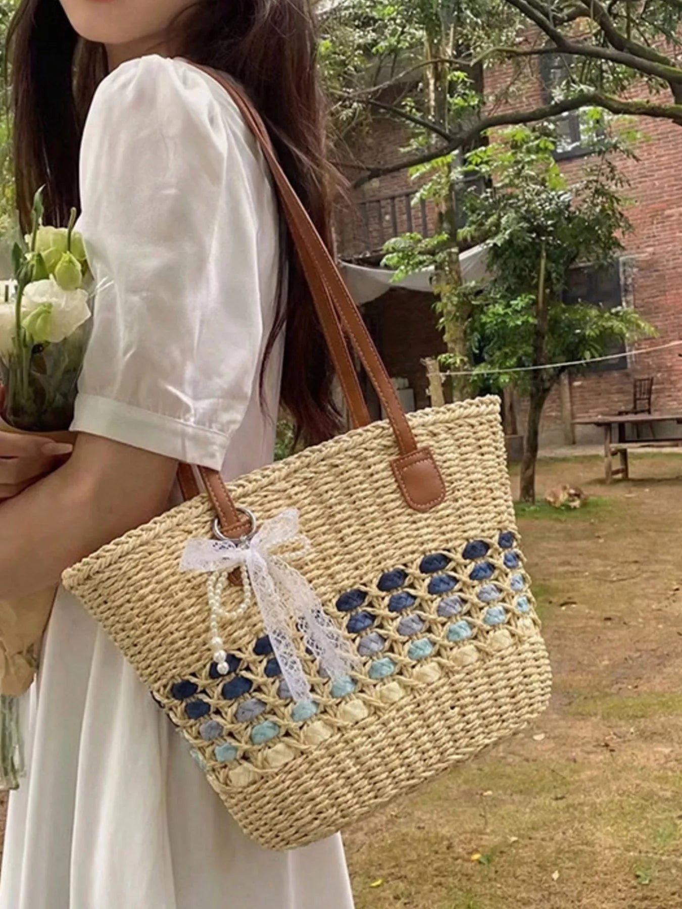 Woven straw shoulder bag with blue lattice panel, brown leather handles, white bow charm