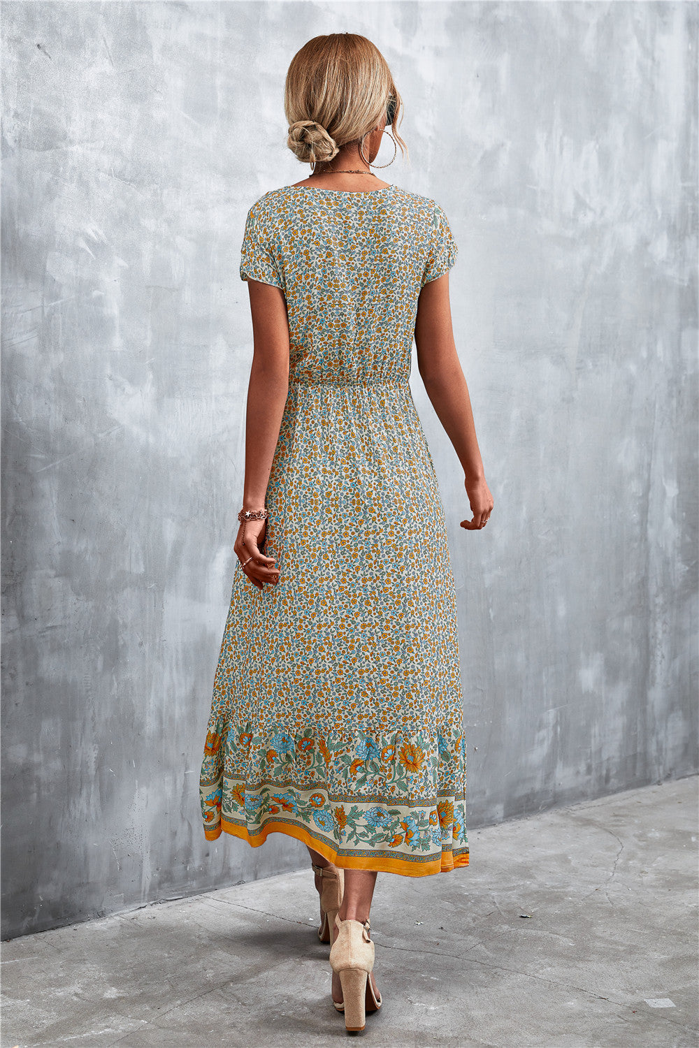 V-neck printed maxi dress with short sleeves, beige base and teal floral hem border, rear view.
