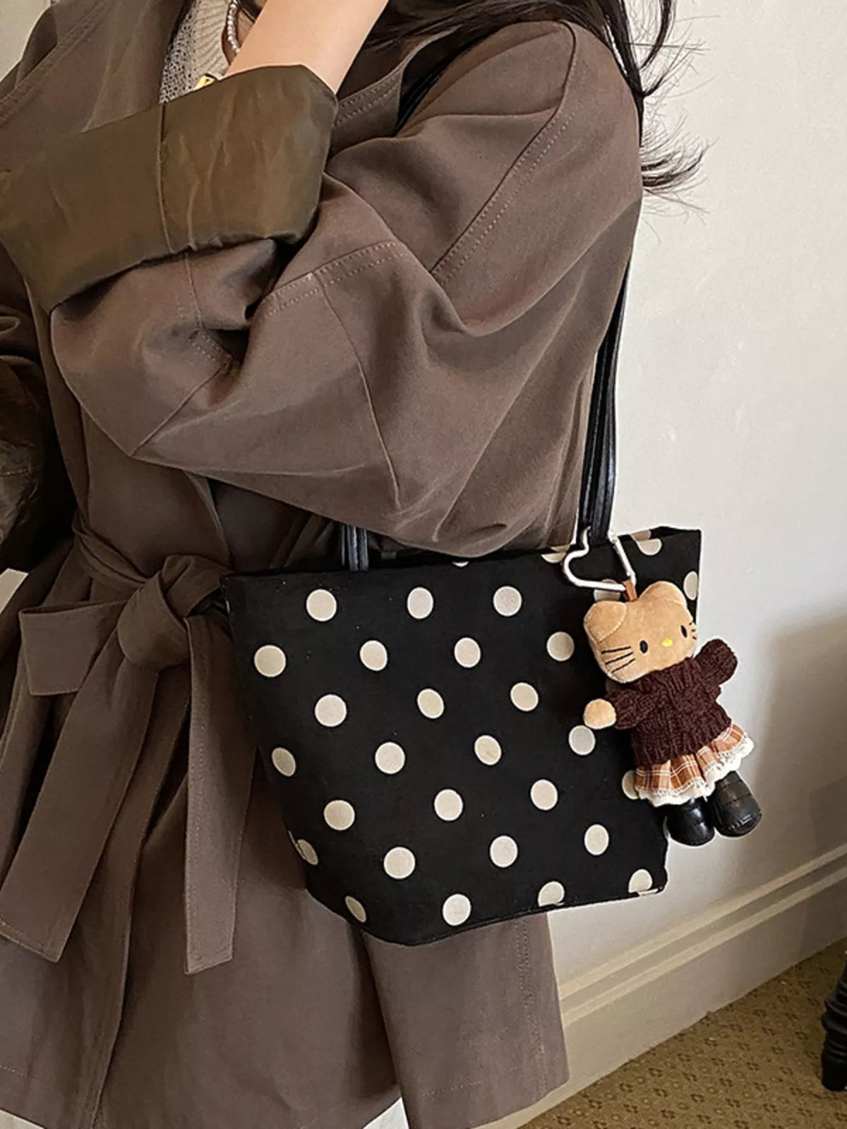 Black suede shoulder handbag with white polka dots and dangling cat accessory charm