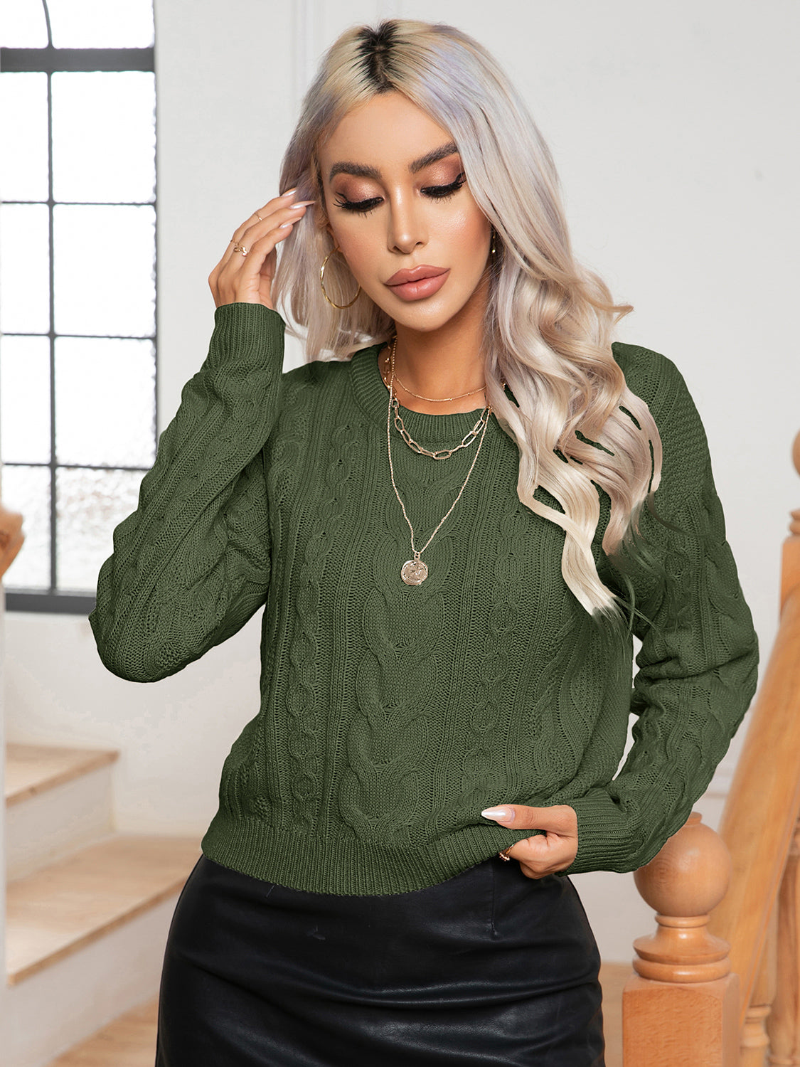 Dark green cable-knit round-neck sweater with long sleeves, cable texture, and ribbed cuffs