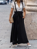 Black wide-leg pants with shoulder straps and bow-tied waist bib front