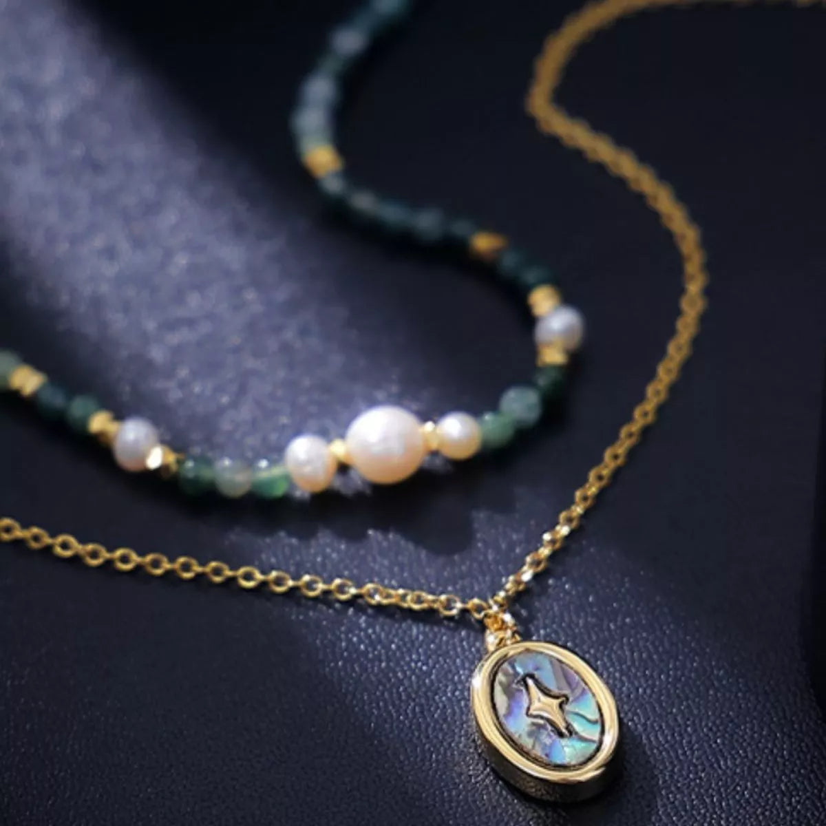 Gold-plated oval pendant over blue-green beaded necklace with round white pearls