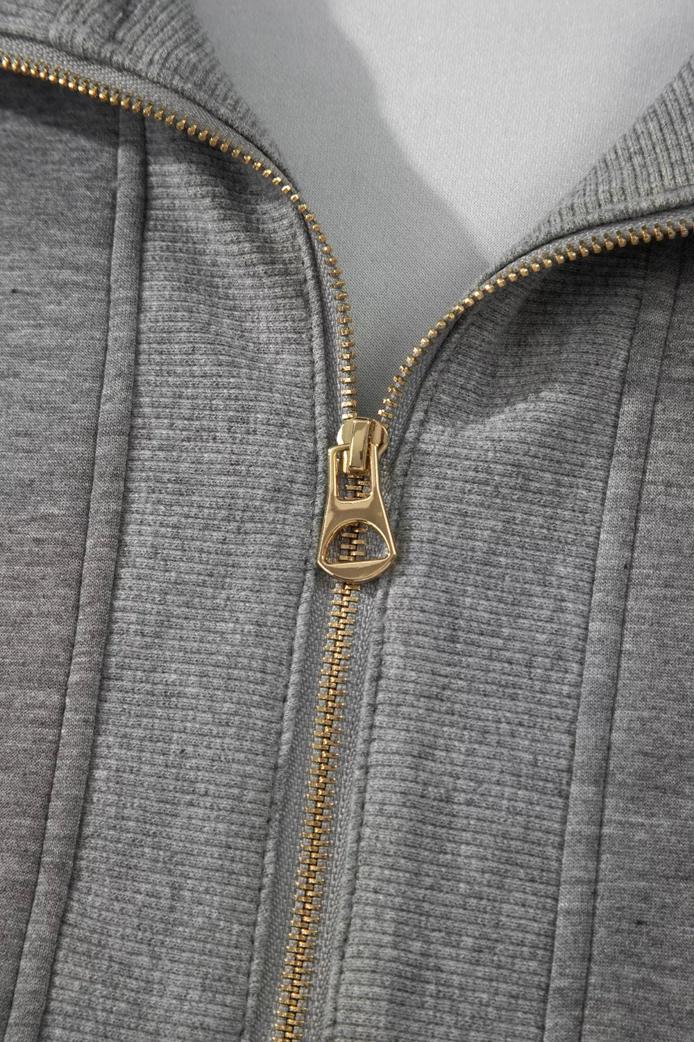 Close-up of dark gray half-zip polo zipper with gold-tone pull and teeth.