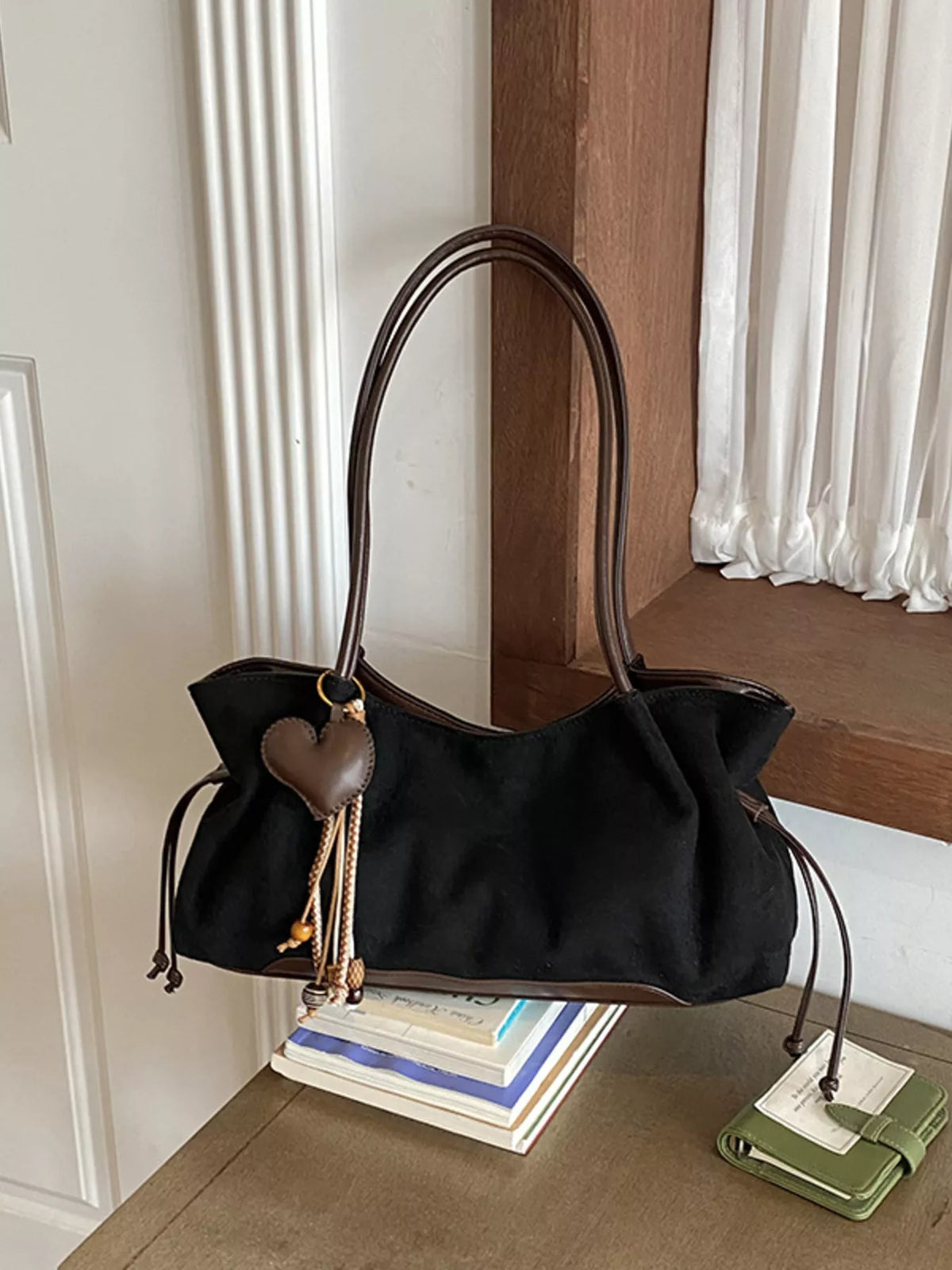 Black suede drawstring shoulder bag with heart charm tassel and braided cord handles