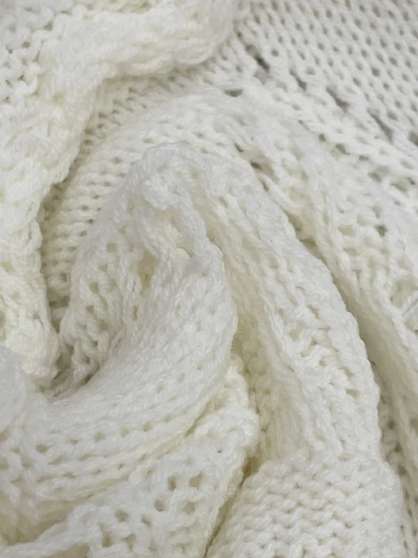 Close-up of white crochet knit with swirling openwork pattern and textured yarn loops