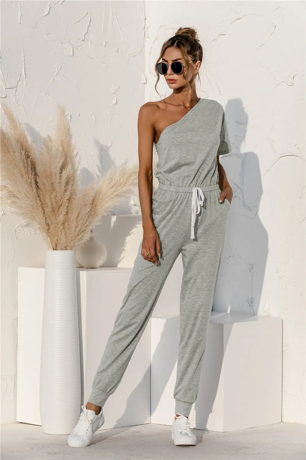 Gray one-shoulder short-sleeve jumpsuit with tie-waist detail and cuffed tapered legs