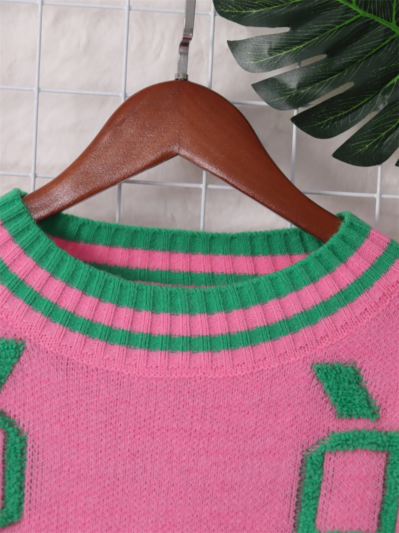 Pink sweater neckline with green-striped ribbed collar and green geometric square detail