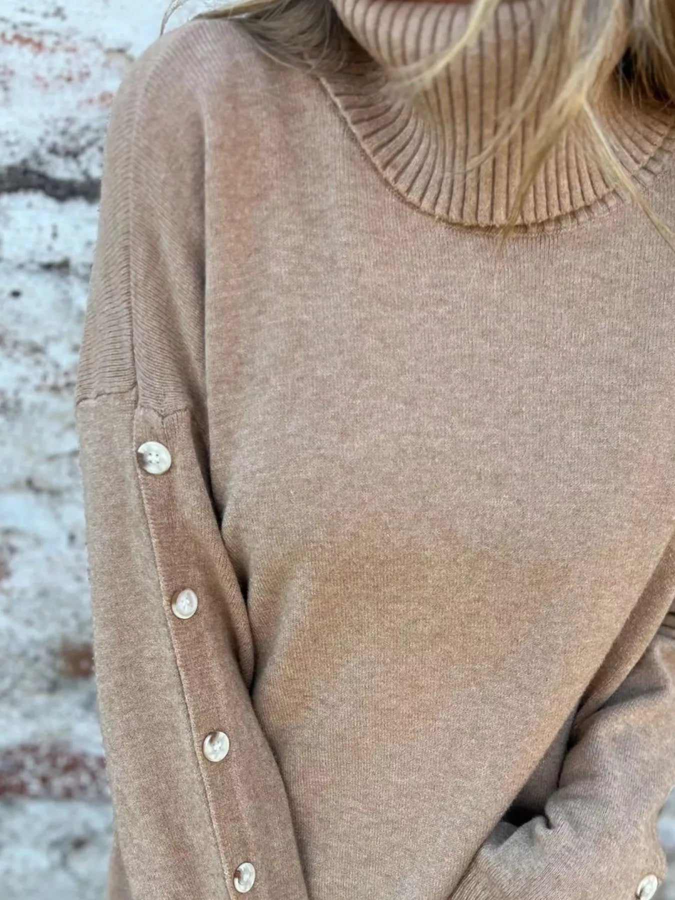 Tan turtleneck sweater close-up with ribbed collar and buttoned sleeve cuff