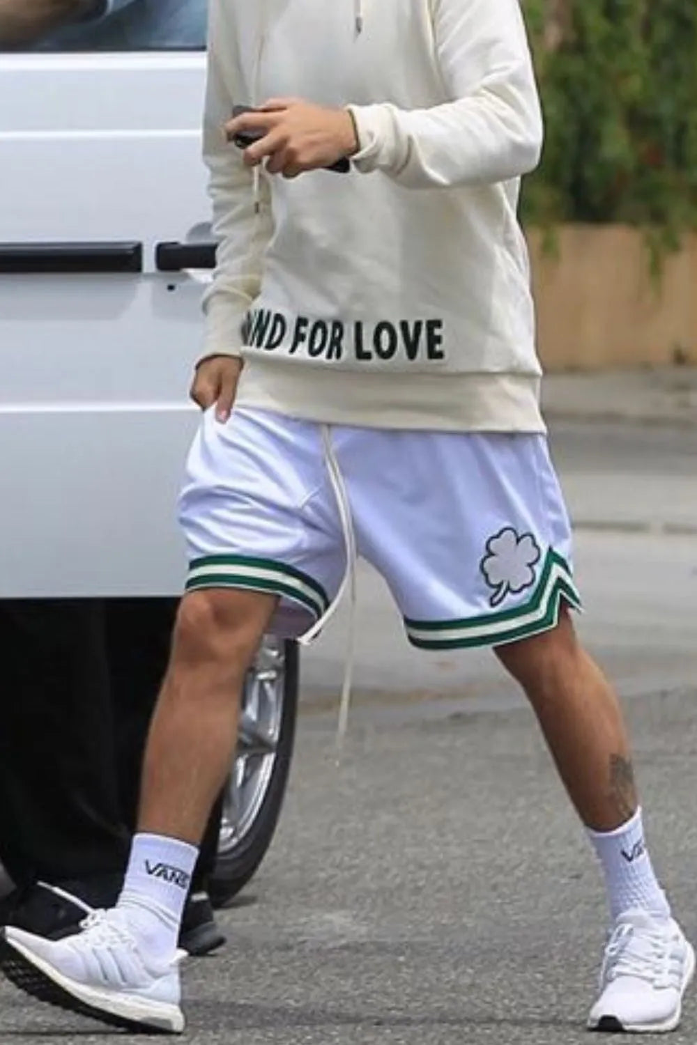White drawstring casual shorts with green trim, side pockets, and clover-style graphic
