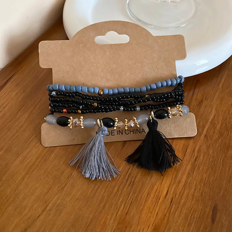 Beaded tassel bracelet with blue and black strands, gold charms, and two tassels