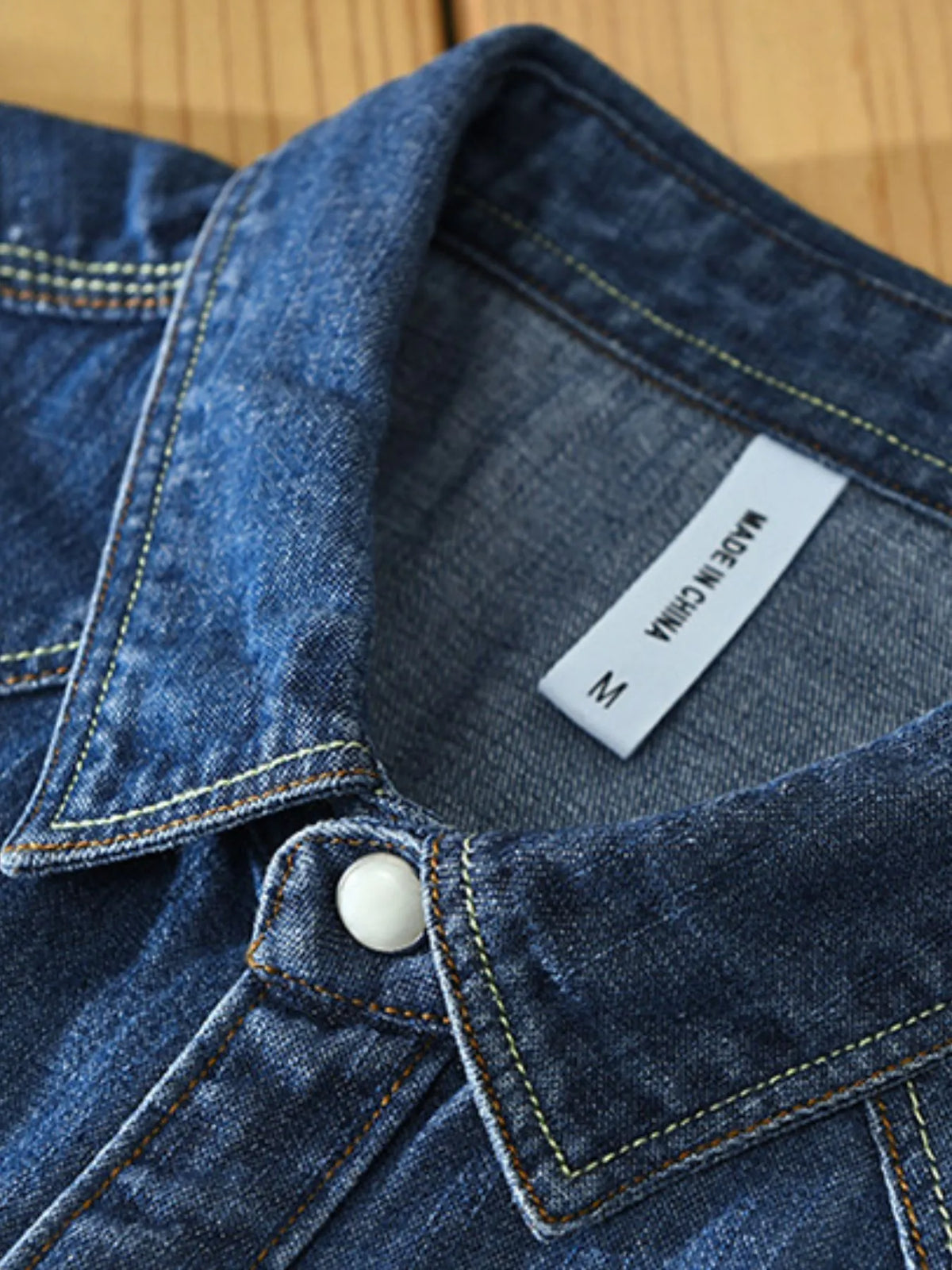 Men's denim button-up shirt neck and button placket close-up in dark blue wash