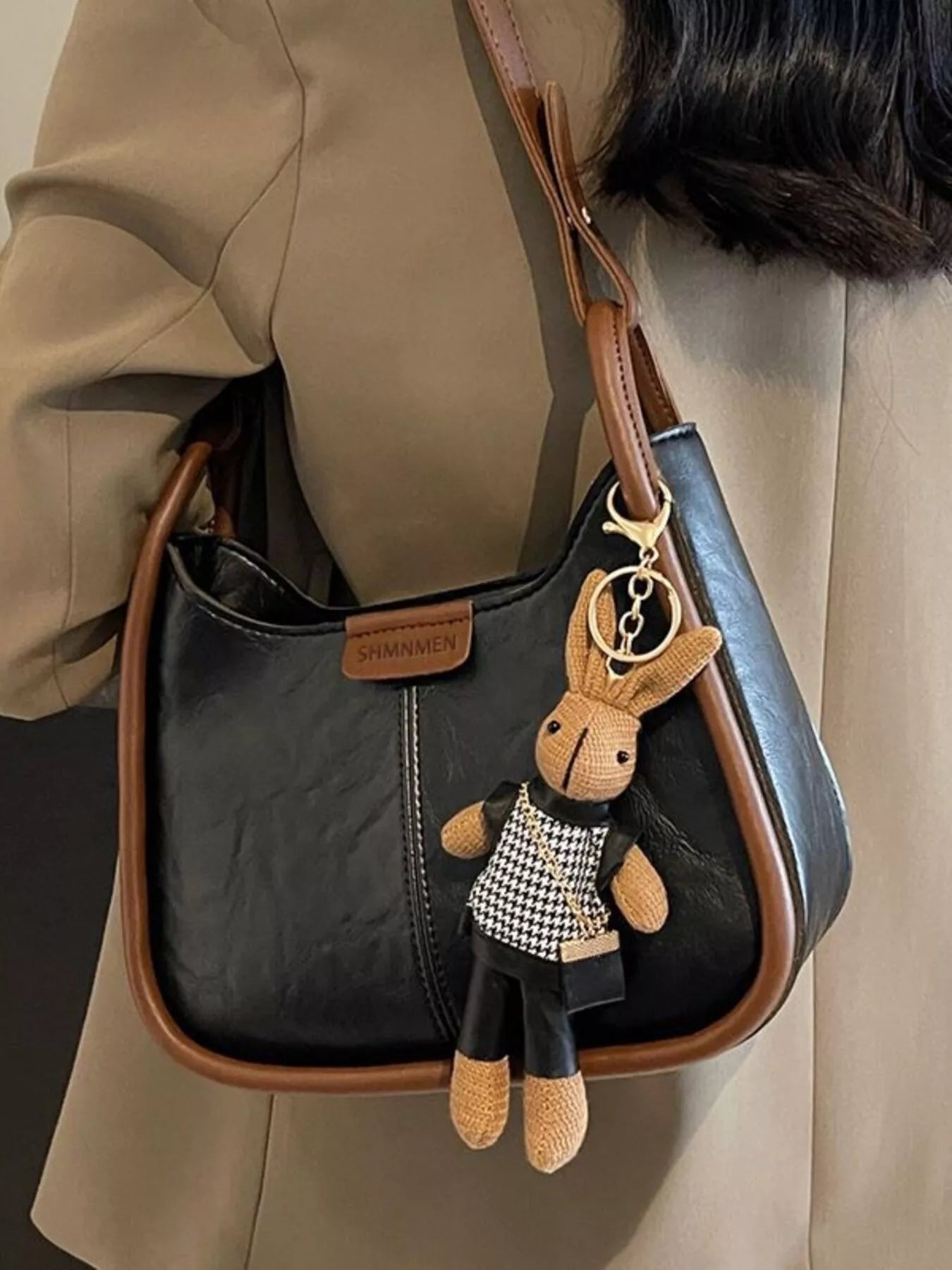 Small adjustable strap shoulder bag in black PU with brown trim and a bunny plush keychain.
