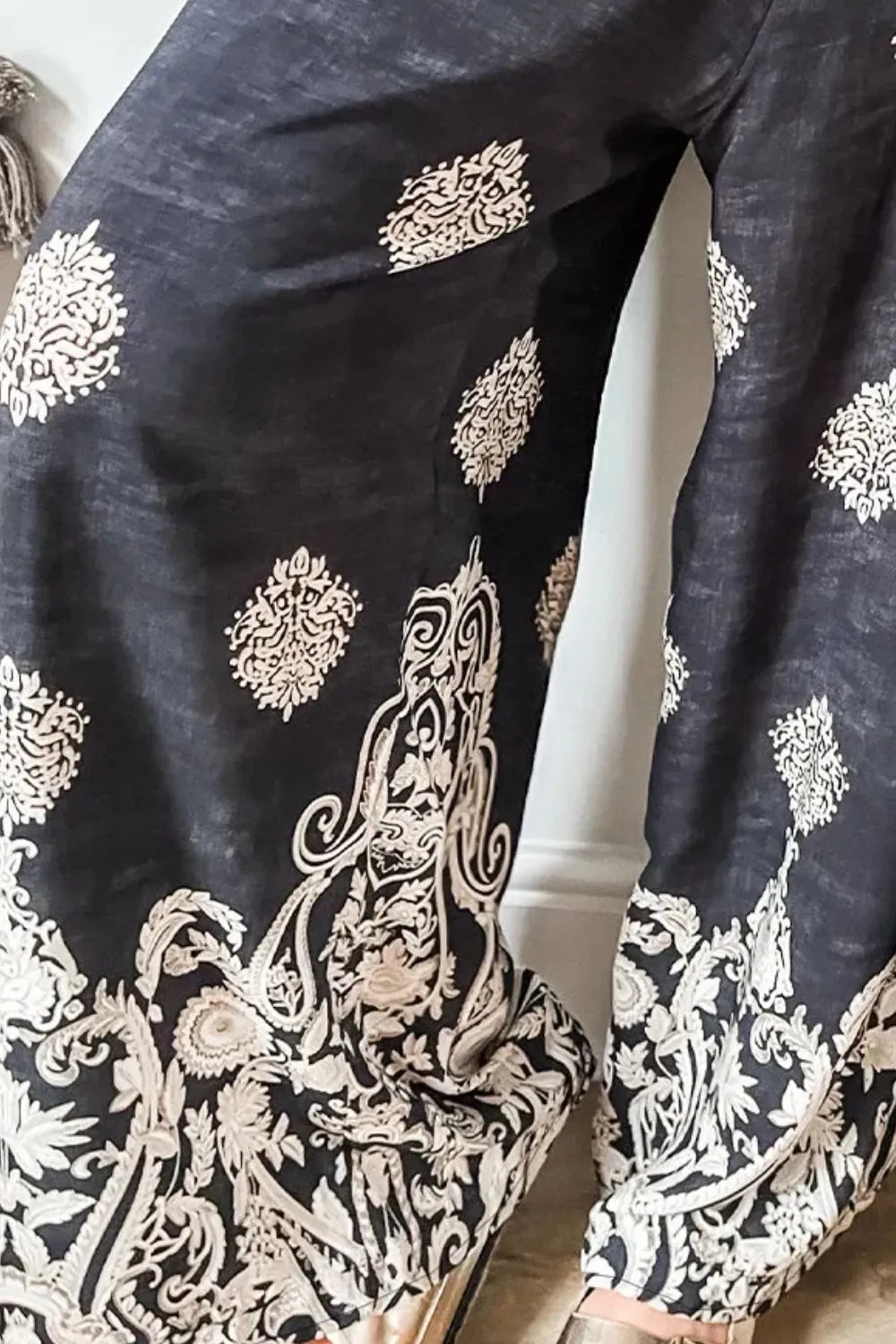 Black wide-leg pants close-up, white paisley-like print along wide hem