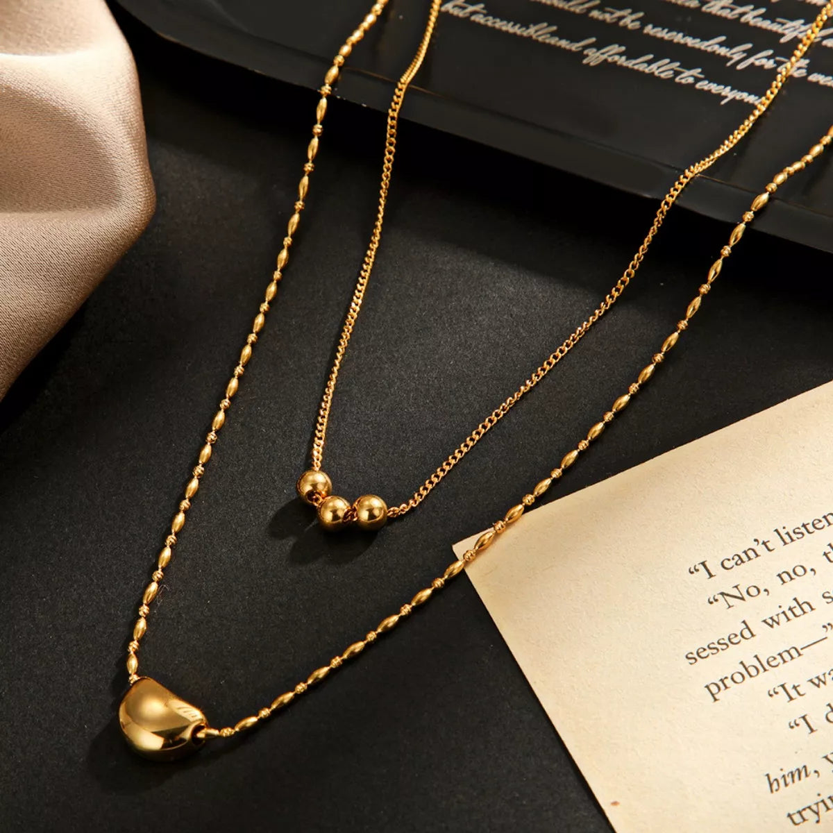 Gold double-layer necklace with heart charm and small bead details, shown on a gift box.