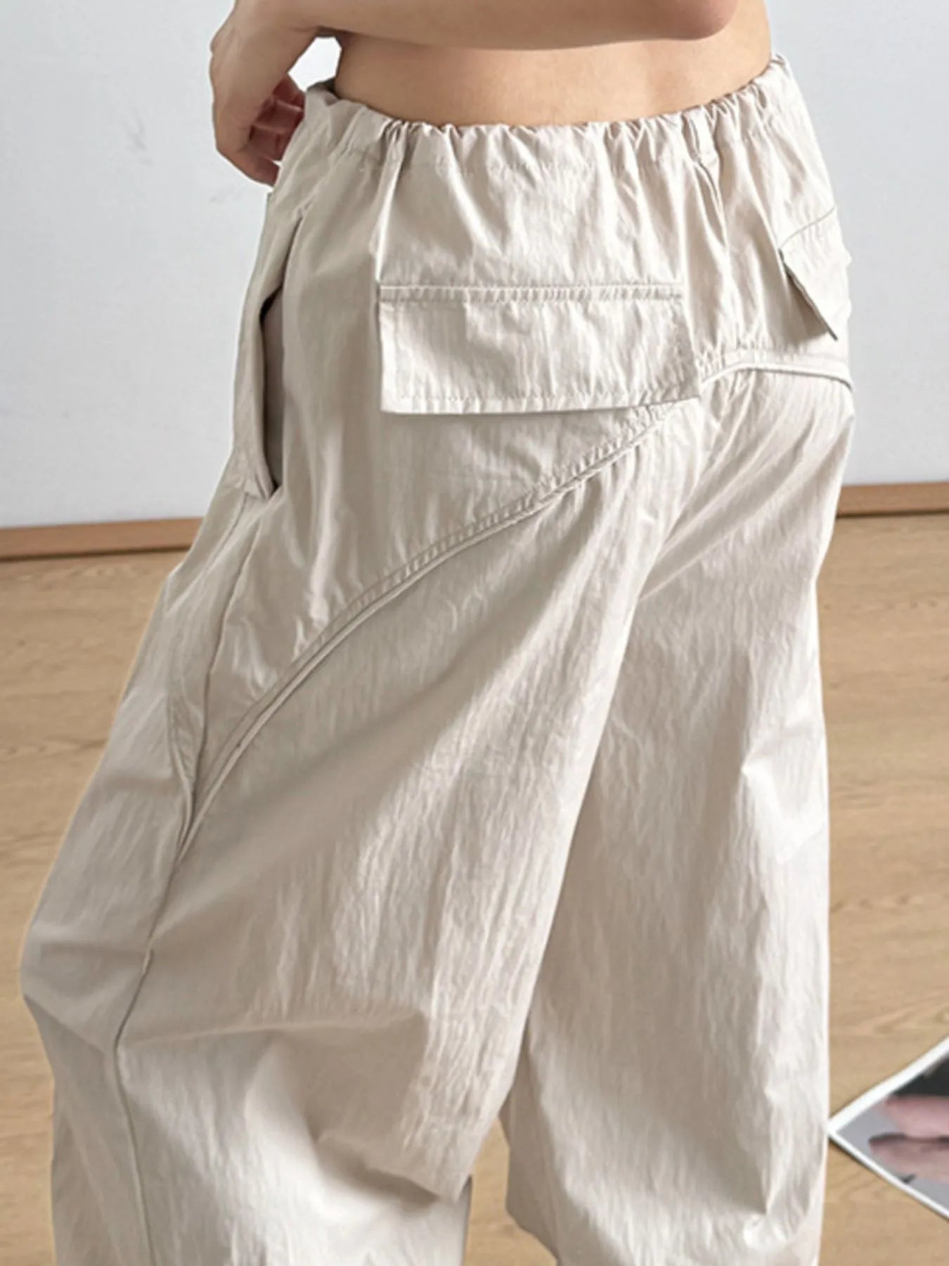 Beige wide-leg cargo-style drawstring pants with layered pocket panel