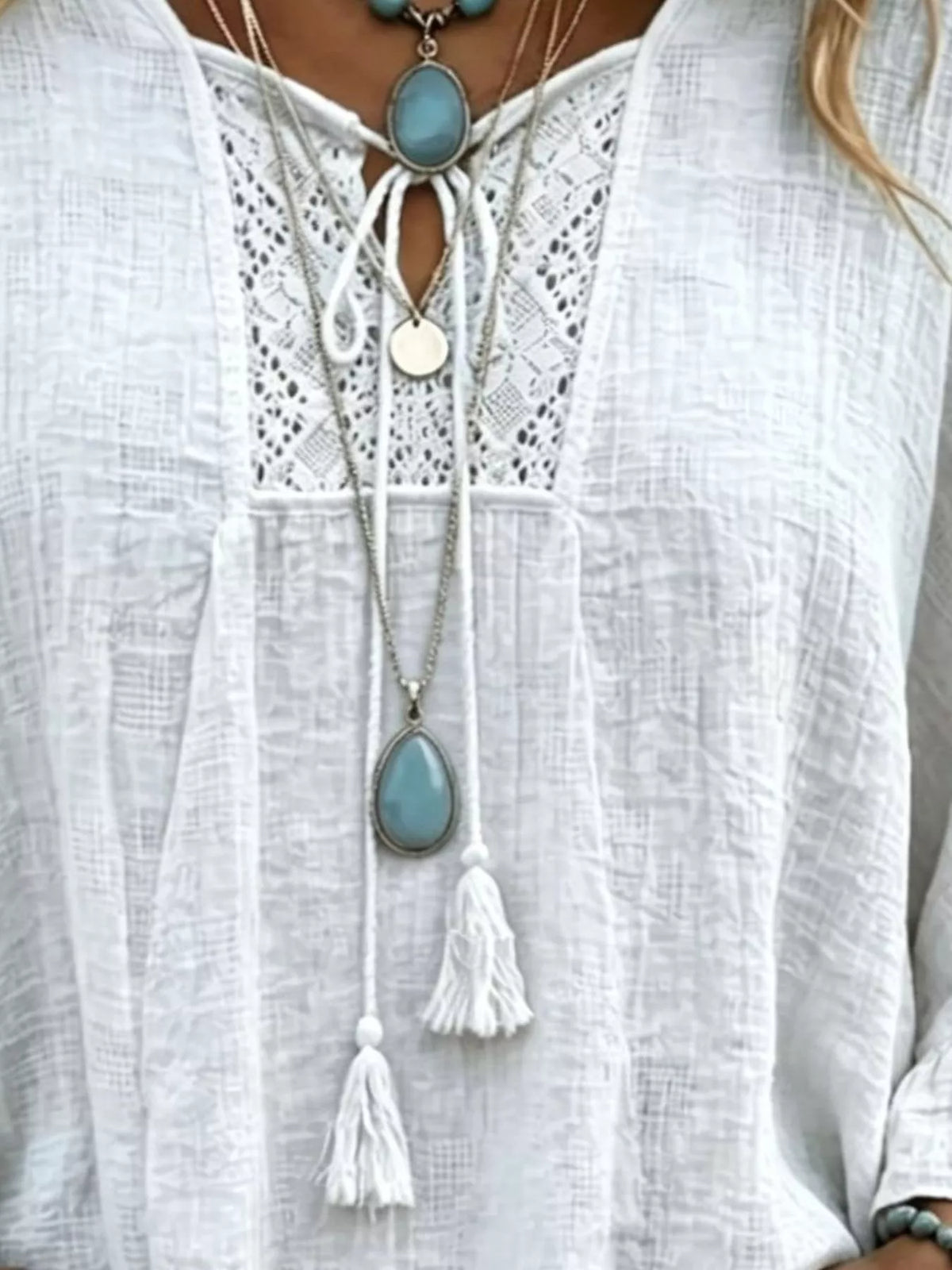 White tie-neck blouse with lace panel and tassel accents at the neckline