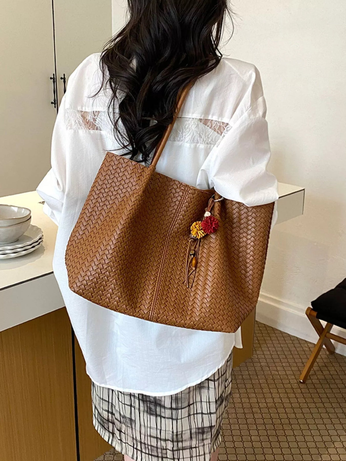 Brown woven vegan leather tote bag with long handles and tassel charm on front
