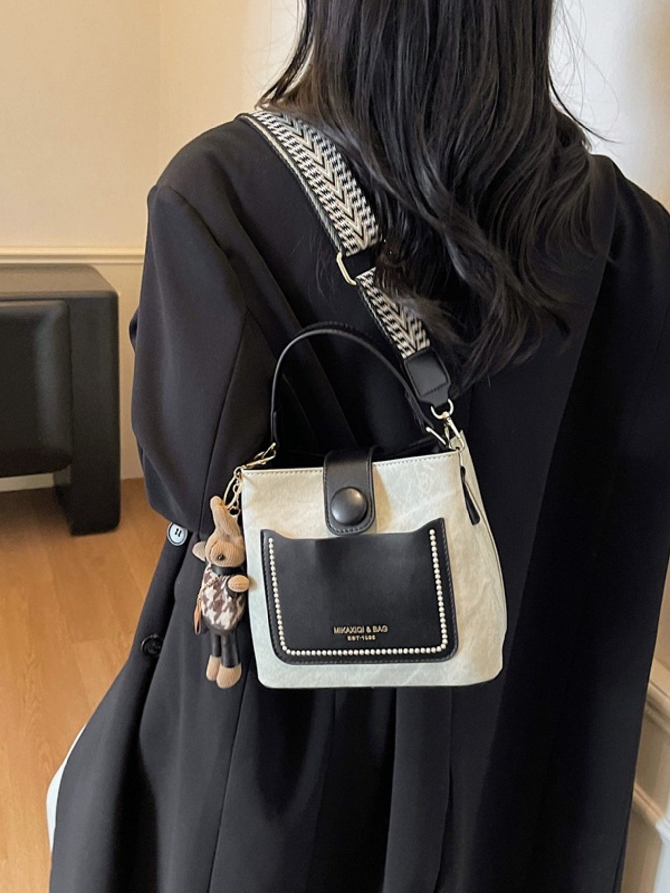 Two-Tone Bucket Crossbody Bag; small PU handbag with beige body, black front pocket, studs, and patterned strap