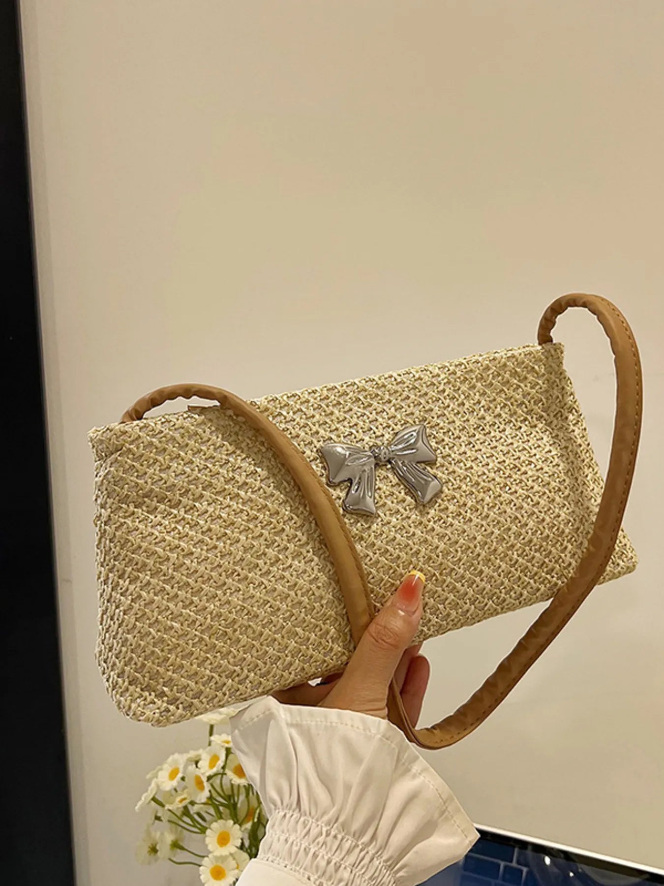 Woven straw shoulder bag with silver bow appliqué and tan handle, rounded flap