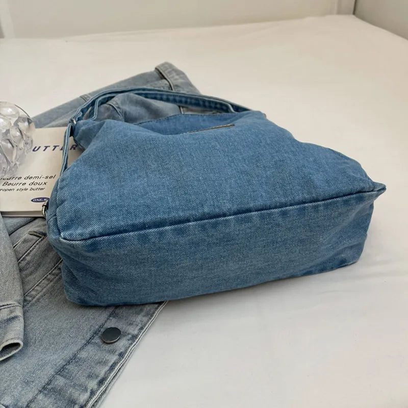 Denim shoulder bag with adjustable strap, blue exterior and wide top panel, no contents