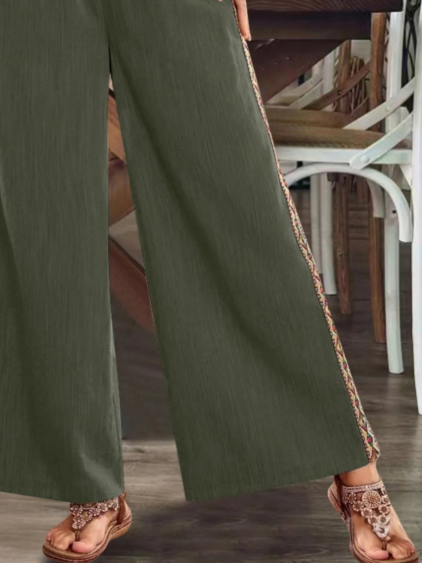Close-up of olive wide-leg pants with embroidered side stripe and wide hem.