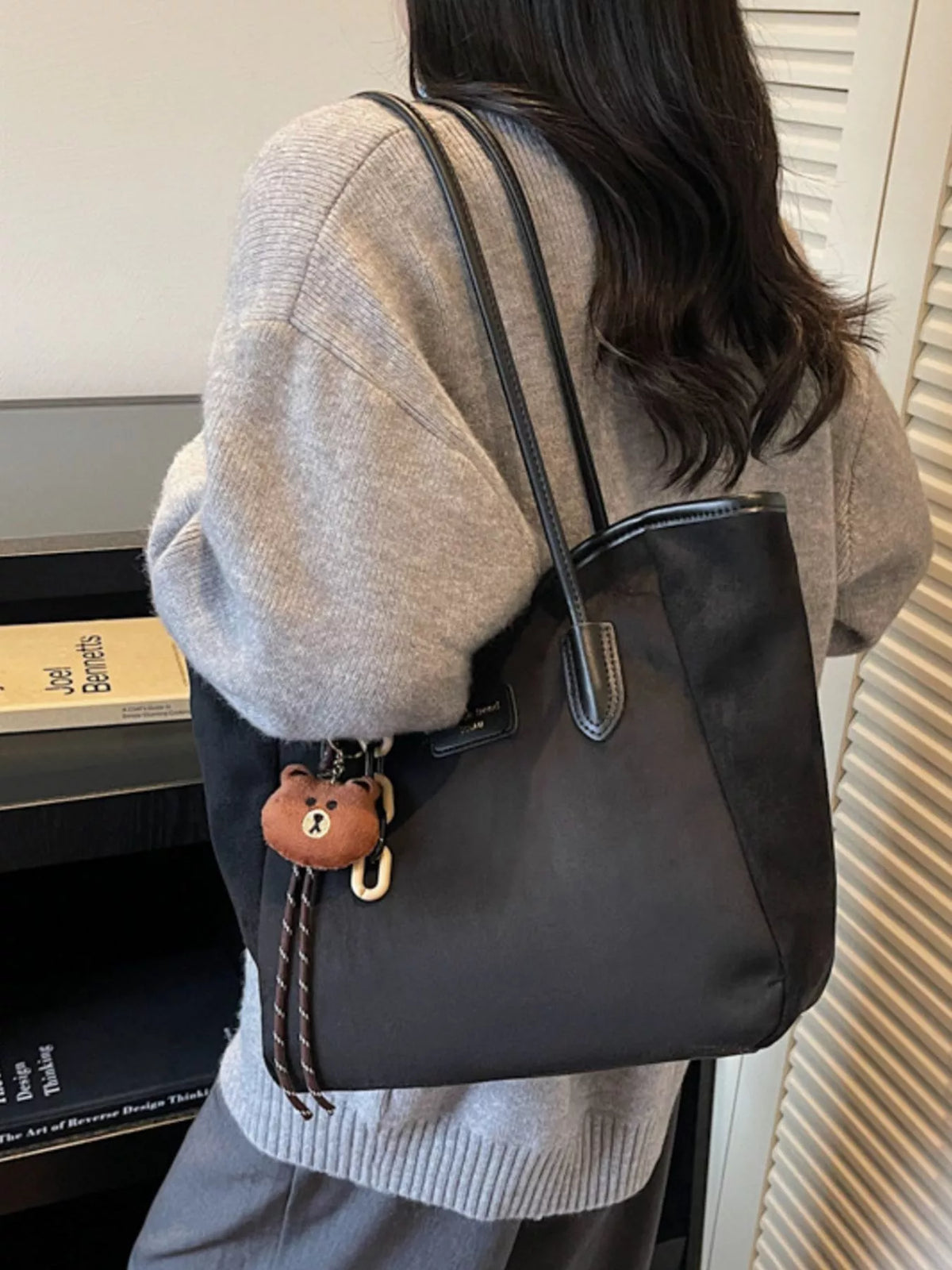 Black suede tote bag with side pocket, zipper top, and bear keychain charm